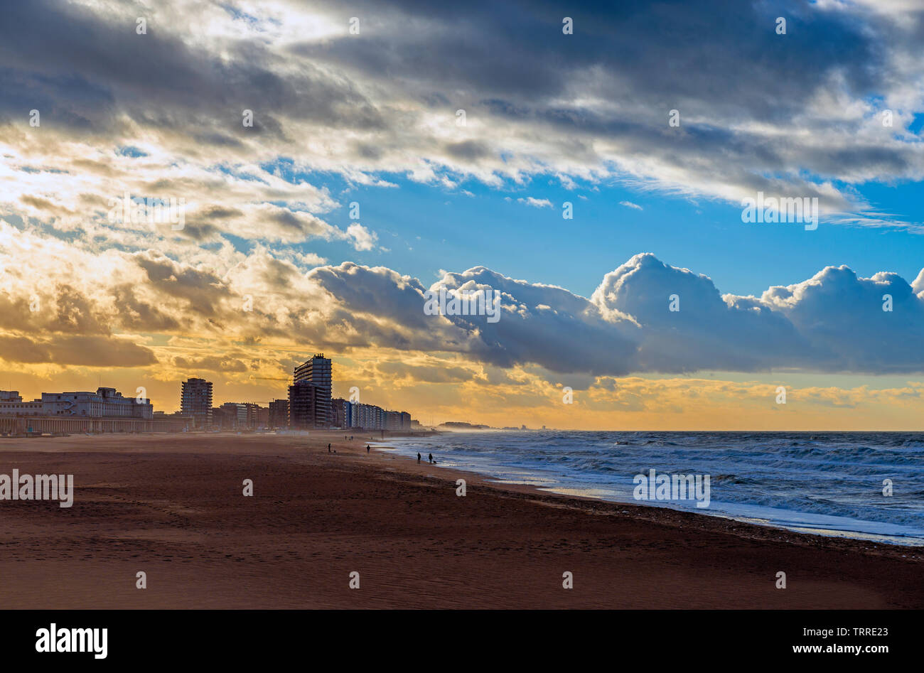 Distanti sagome di persone a piedi lungo la spiaggia di Oostende città al tramonto dal Mare del Nord, Fiandre Occidentali, Belgio. Foto Stock