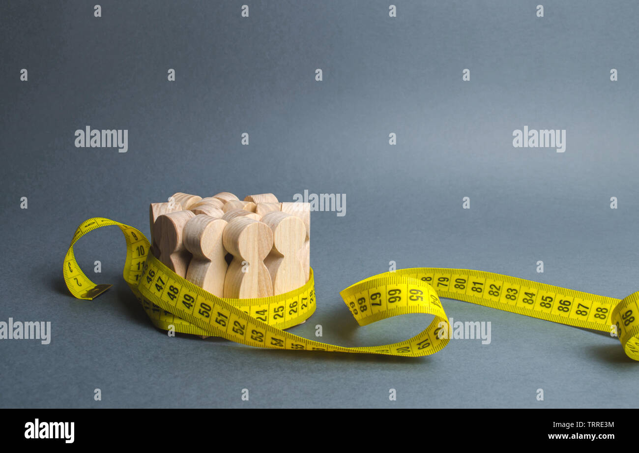 Una folla di figure in legno afferrata dal nastro di misurazione. Informazioni statistiche, misura del numero, le tendenze di crescita della popolazione. Scienze sociali. Foto Stock