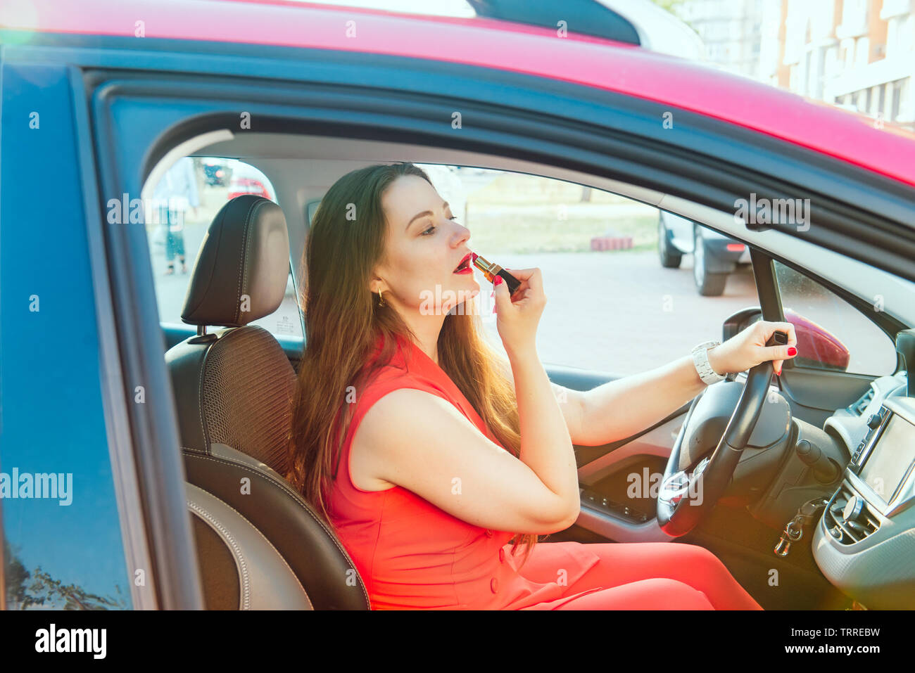 Vista laterale giovane donna guardando nel retrovisore e putting fanno in auto. Moderna vita occupato. bella ragazza seduta nel sedile di guida della vettura applicando Foto Stock