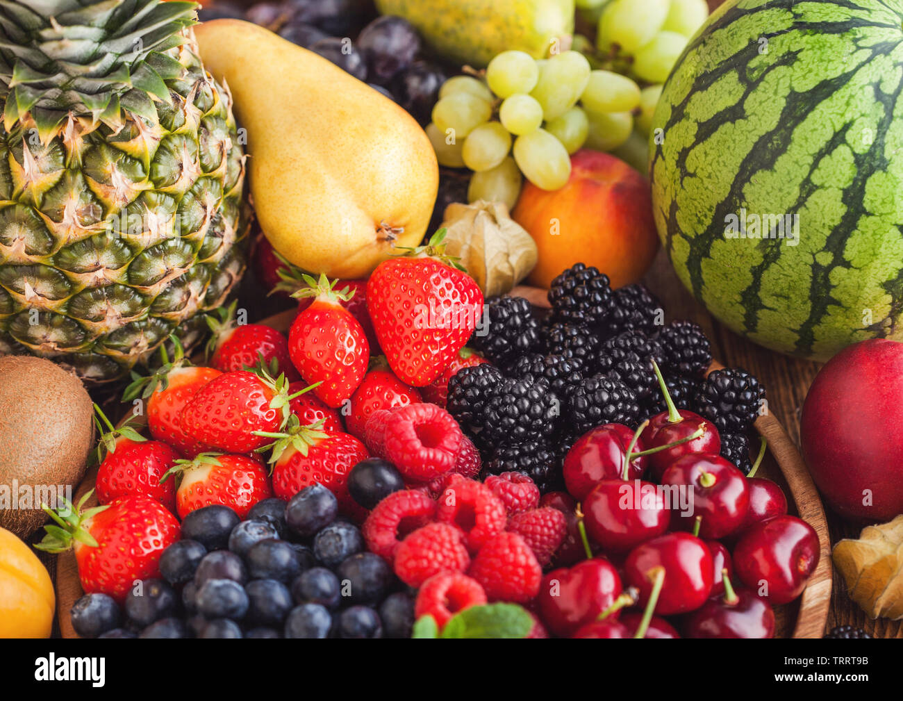 Fresca estate organico mix di frutti di bosco nel vassoio di legno e frutti esotici su sfondo di legno. Lamponi, fragole, mirtilli, more e cherr Foto Stock