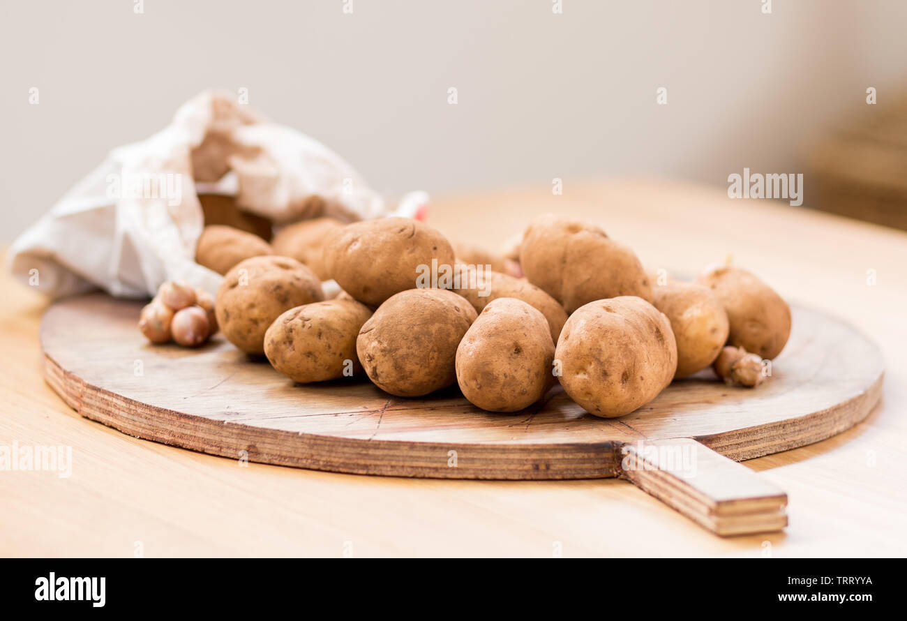 Patate acquistati direttamente dall'agricoltore di cadere fuori del sacco su un legname tagliere Foto Stock