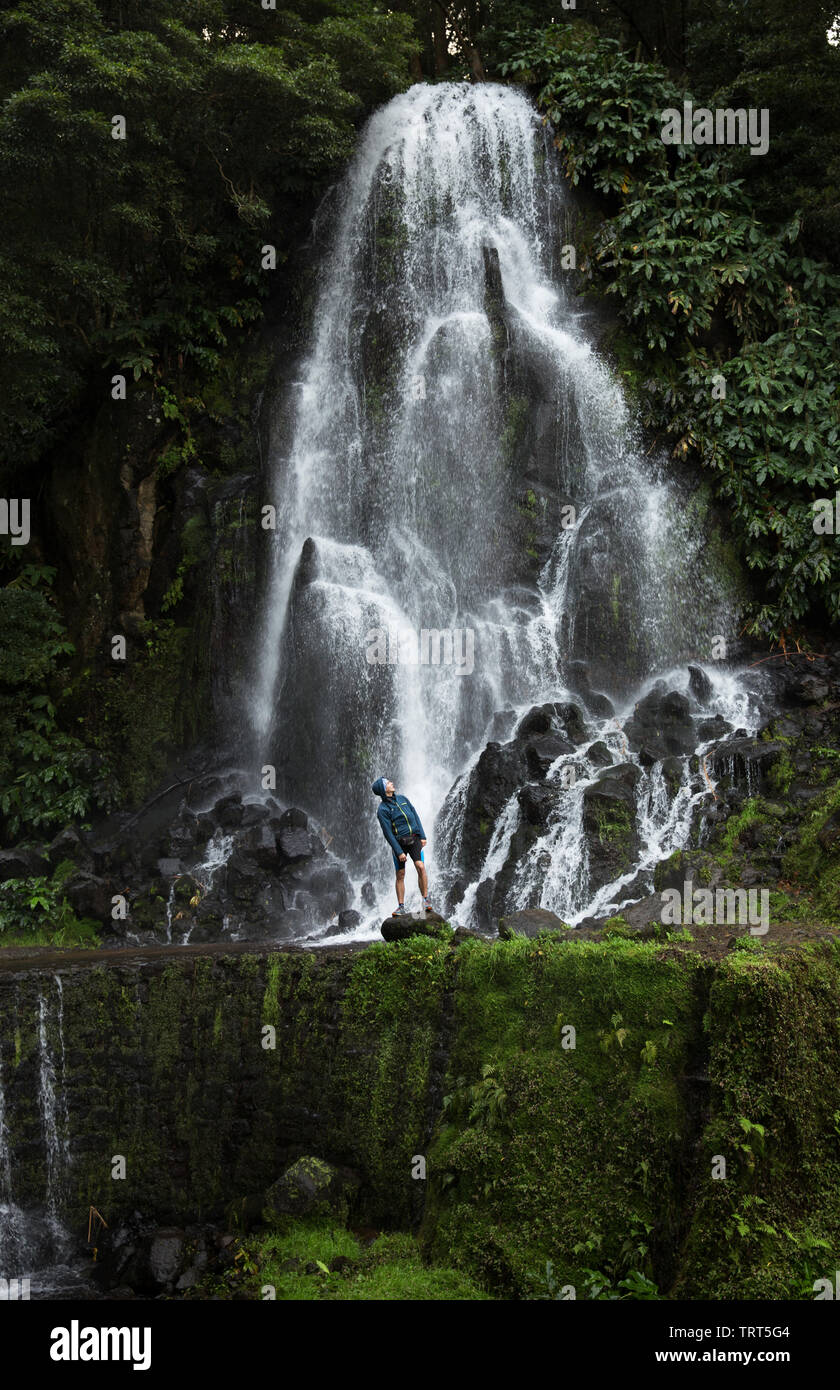 Un uomo esplora nuovi, magici e fantastici luoghi in tutto il mondo è di fronte ad una cascata, circondato da natura e sta guardando verso l'alto e rilassarsi. Foto Stock