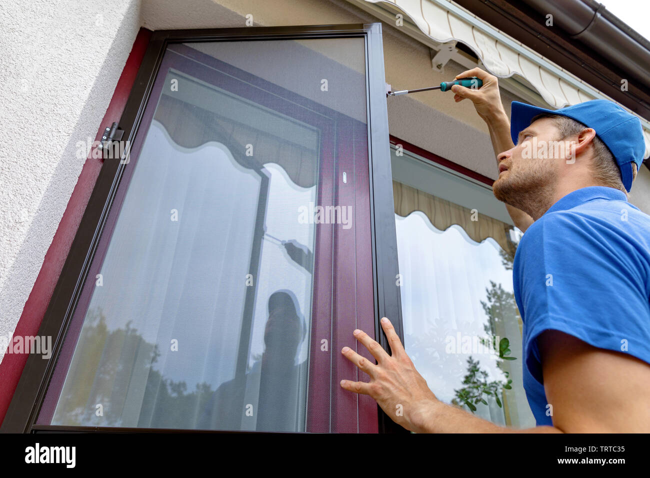L'uomo installazione zanzariera schermo di filo sulla terrazza porte Foto Stock