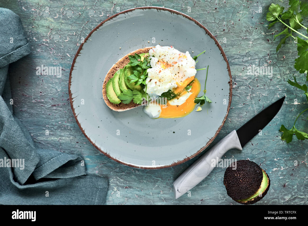 Avocado sandwich con pane scuro, tagliata a fette di avocado e uovo in camicia, piatto giaceva sul turchese sfondo rustico Foto Stock