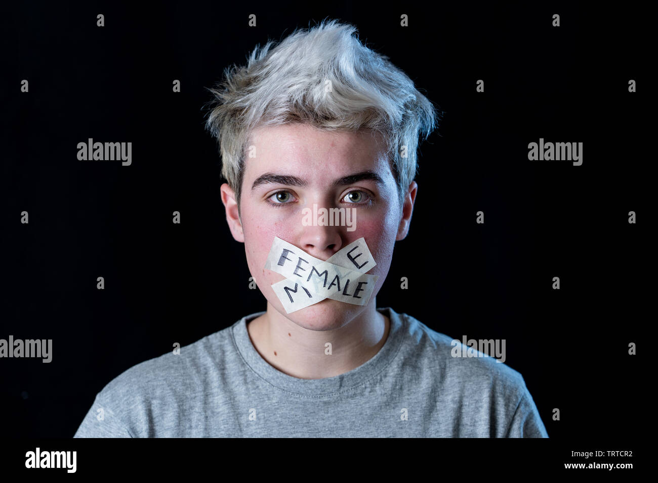 Transgender teenager con la bocca chiusa a tenuta su nastro con parole maschio e femmina scritto in tabù sociale delle diversità di genere concetto. Trans ragazzo non in grado di c Foto Stock
