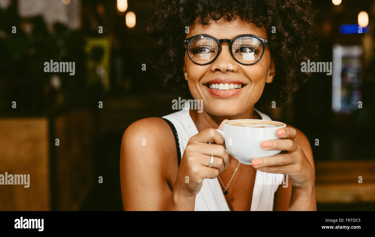 Donna africana con una tazza di caffè presso il cafe. Femmina presentando un caffè e guardare lontano. Foto Stock