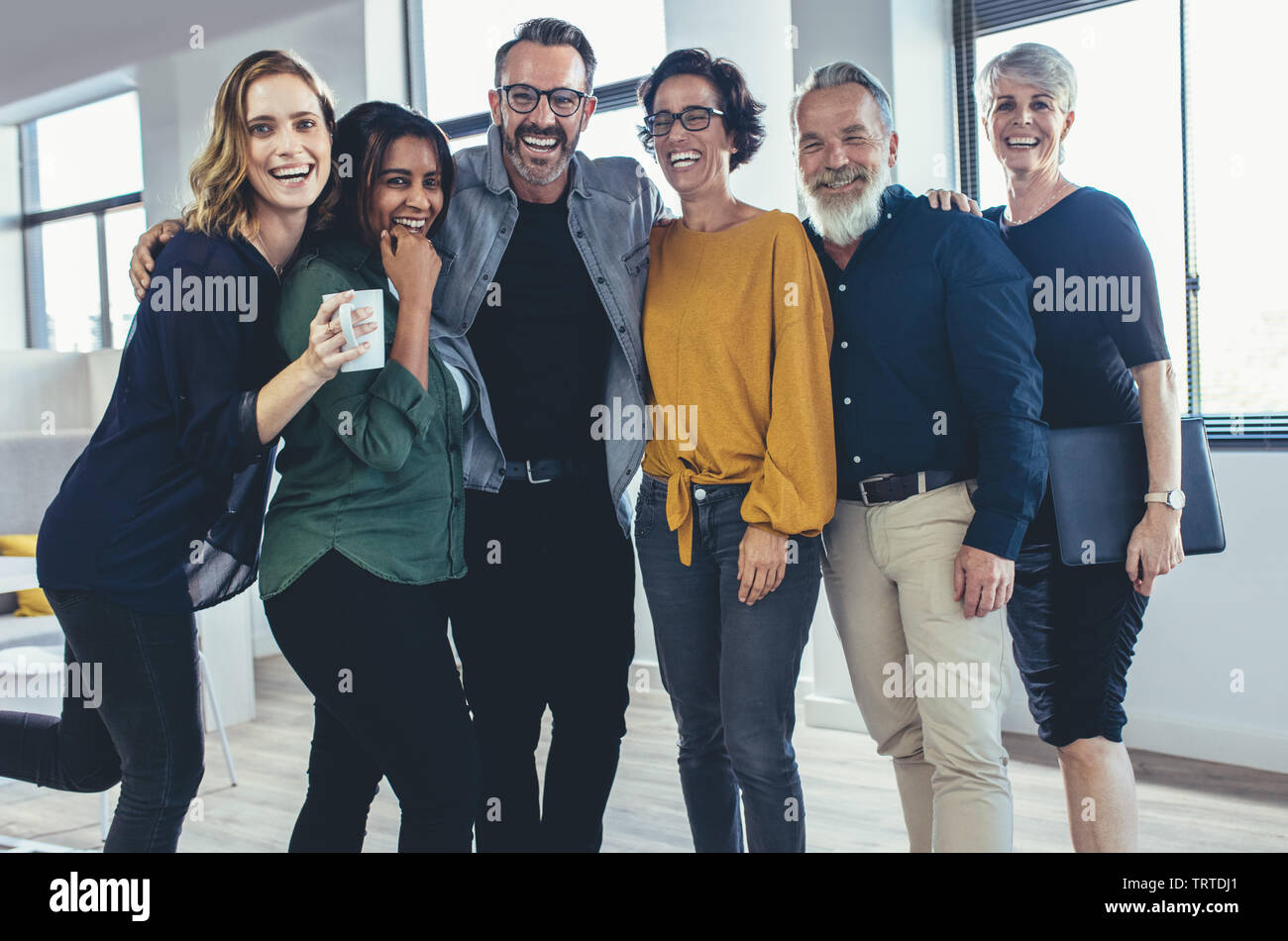 Allegro business persone in piedi insieme e ridere. Il team di professionisti di aziende guardando la fotocamera e sorridente. Foto Stock