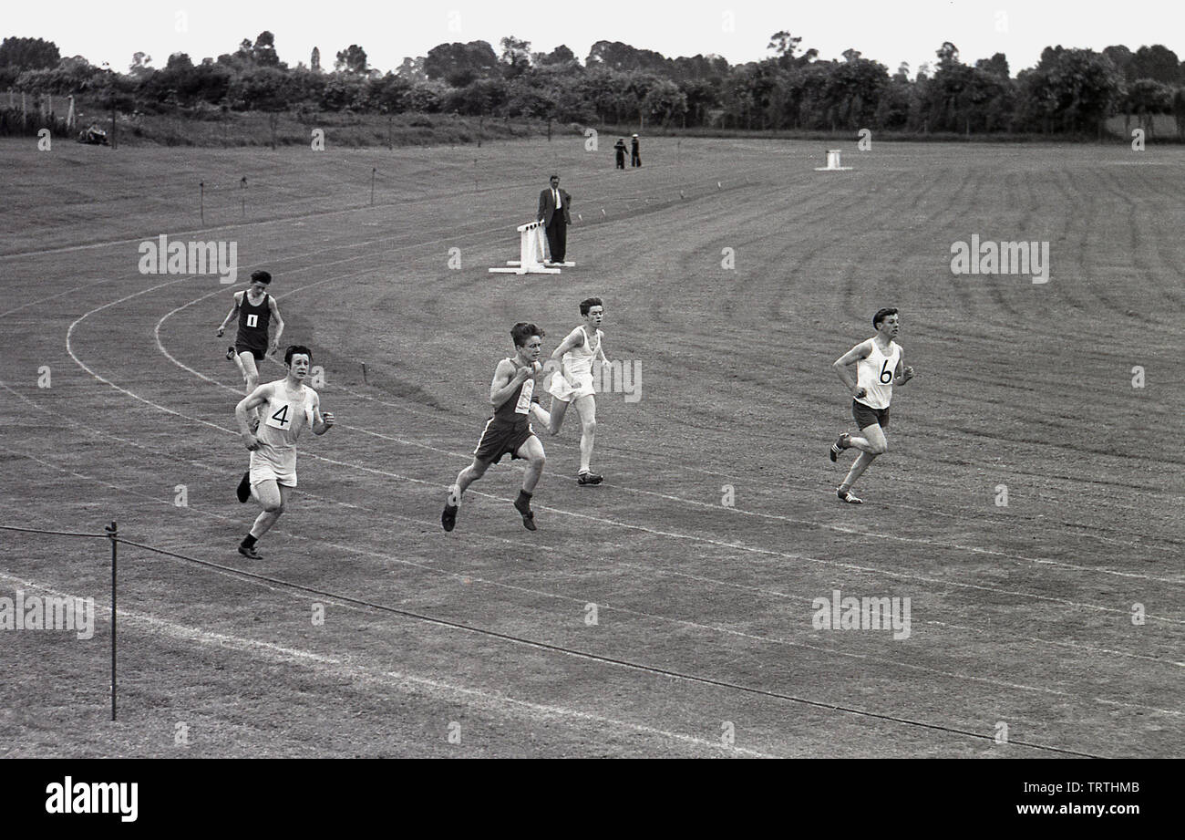 Degli anni Cinquanta, storico, maschi giovani atleti impegnati in una gara di corsa al di fuori su una pista in erba in un ampio campo, Inghilterra, Regno Unito. Foto Stock