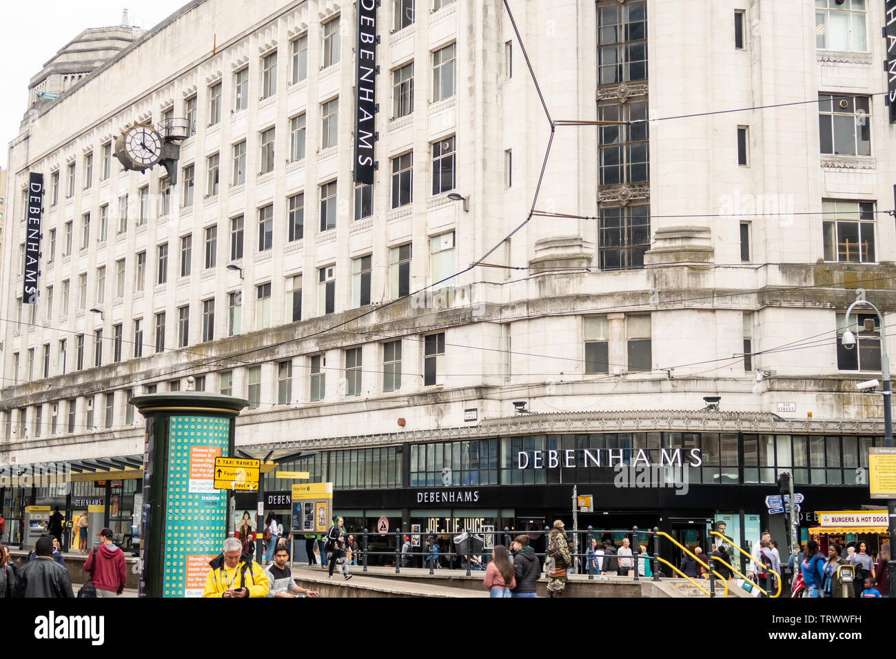 Le persone camminano davanti al negozio Debenhams (l'edificio Rylands) & Market Street fermata del tram, Manchester, Inghilterra, Regno Unito Foto Stock