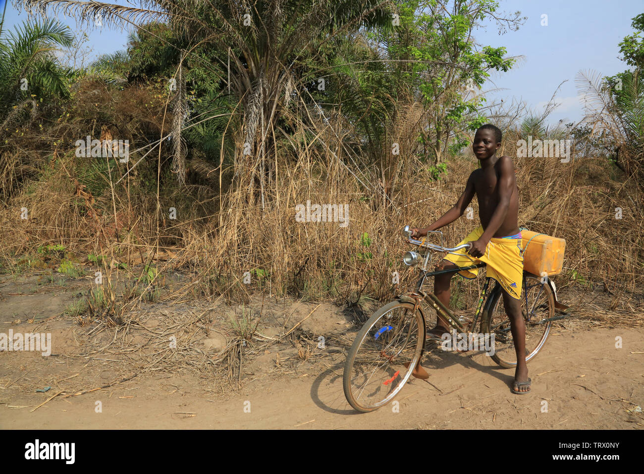Jeune togolais en vélo dans la brousse rapportant de l'eau. Dtacha. Il Togo. Afrique de l'Ouest. Foto Stock