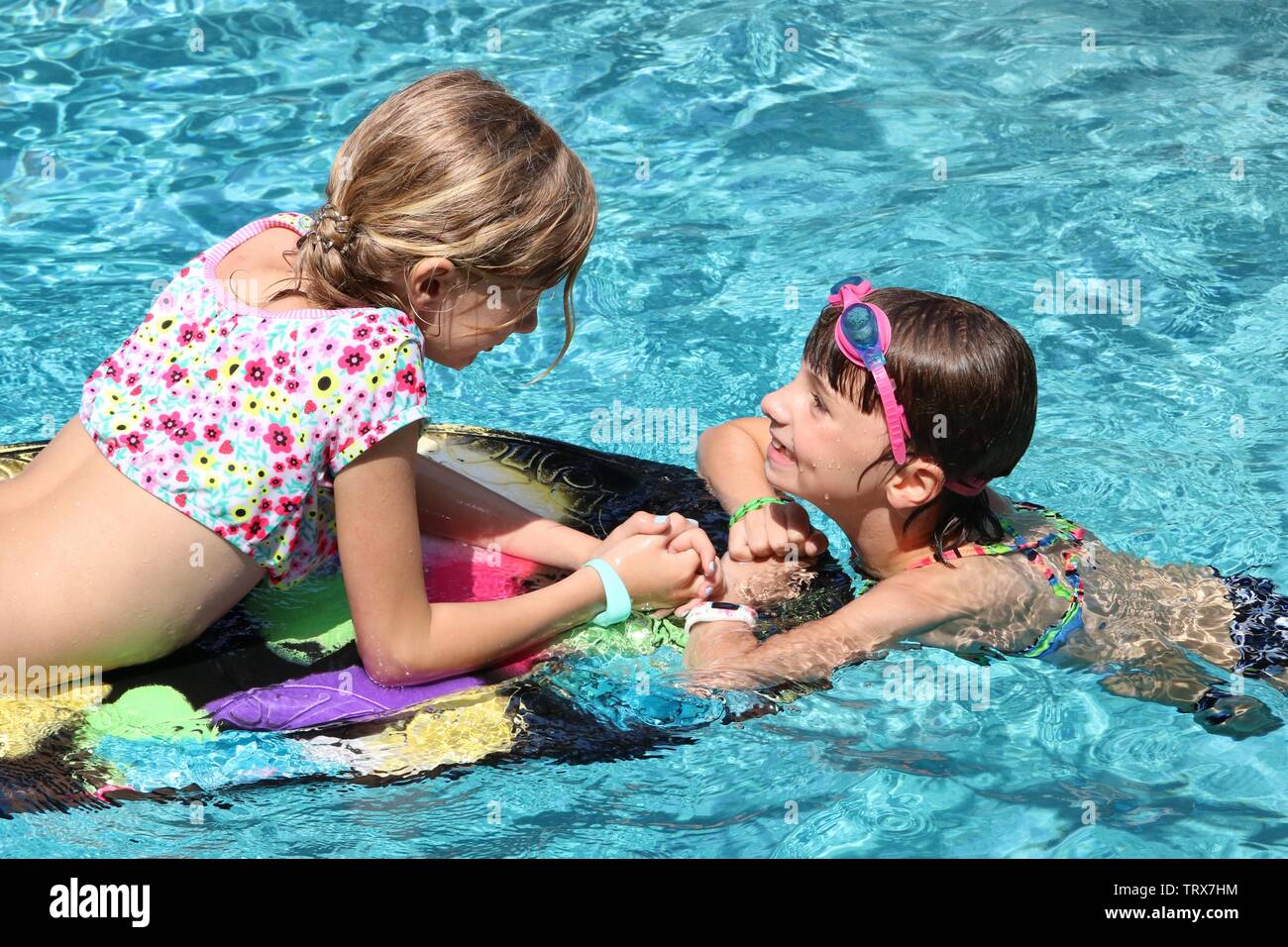 Due ragazze su kickboard in piscina felicemente guardando ogni altro Foto Stock