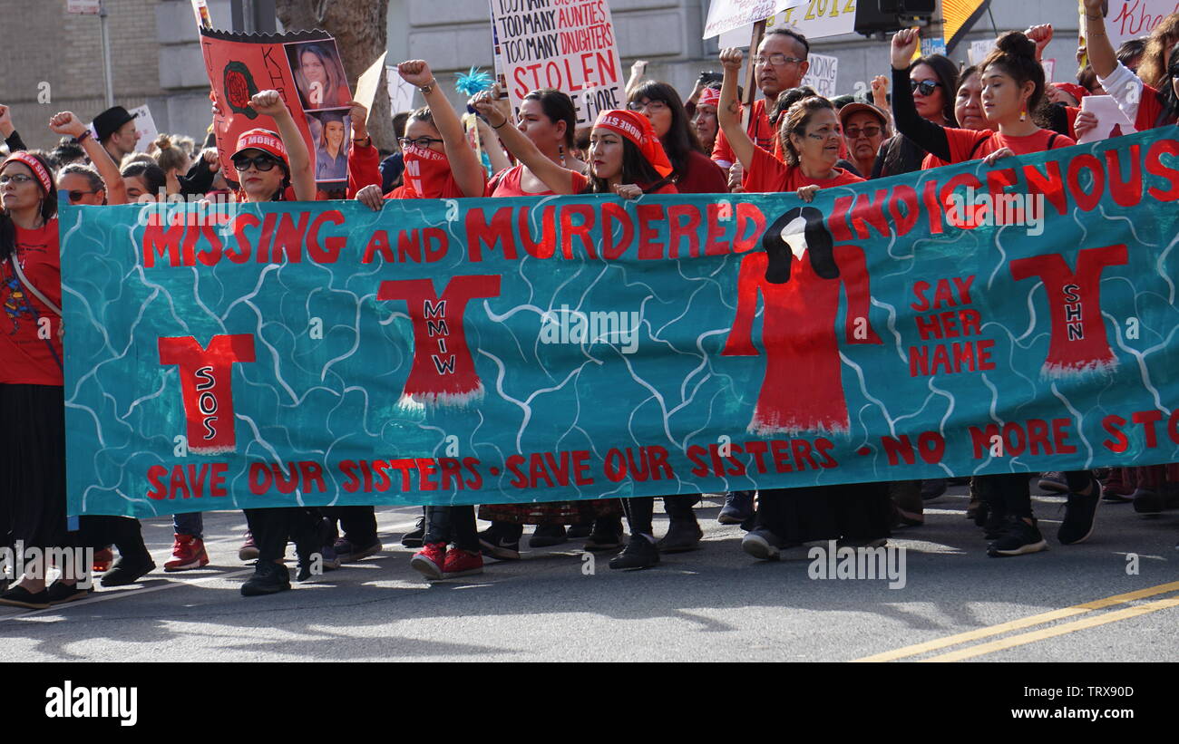 Gli indigeni o nativi americani le donne in marcia con un banner con i pugni in aria. 2019 Donna Marzo, Market Street, San Francisco, California, Stati Uniti d'America. Foto Stock