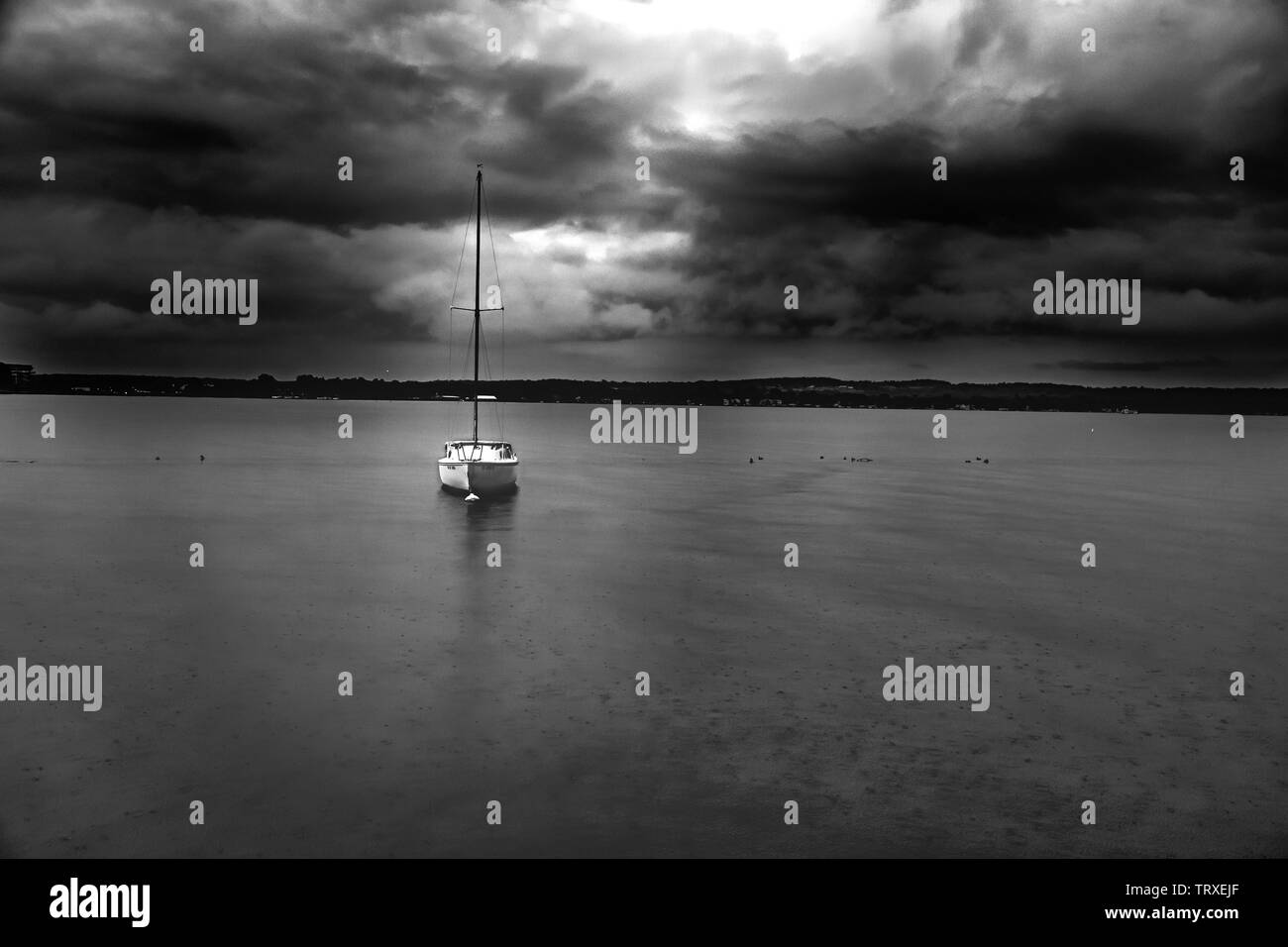 Piccola barca a vela floating sotto minaccioso cielo tempestoso come inizia a piovere. Foto Stock