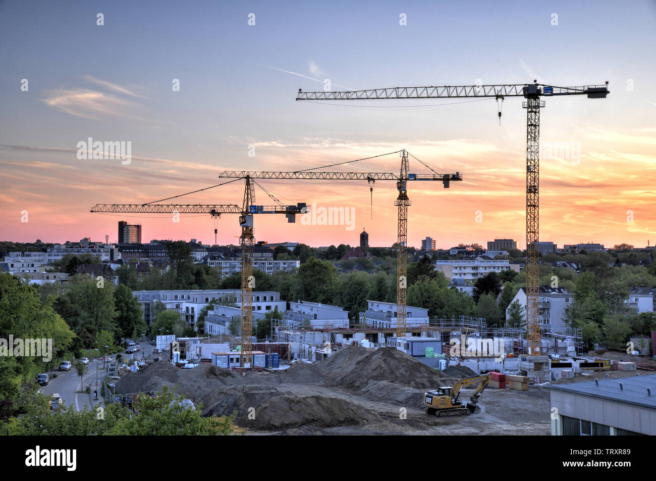 Uebersichtsaufnahme einer Baustelle in Essen NRW zur blauen Stunde mit drei in den Himmel ragenden Baukraenen. Foto Stock