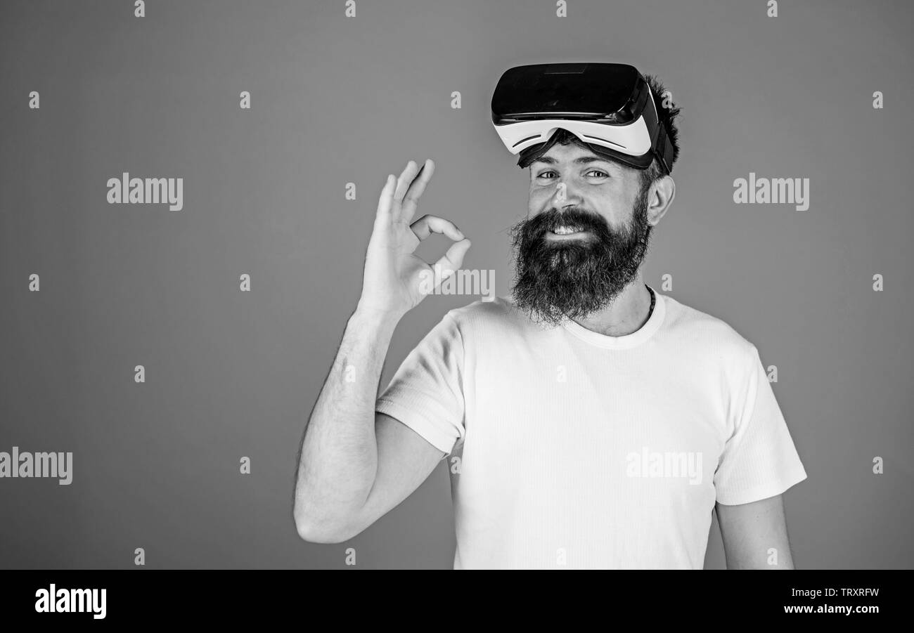 L'uomo con la barba lunga e un ampio sorriso sul volto felice che mostra OK gesto. Barbuto enginner test nuovo modello di VR cuffia digitale il concetto di progresso. Hipster con barba alla moda isolato su sfondo blu. Foto Stock