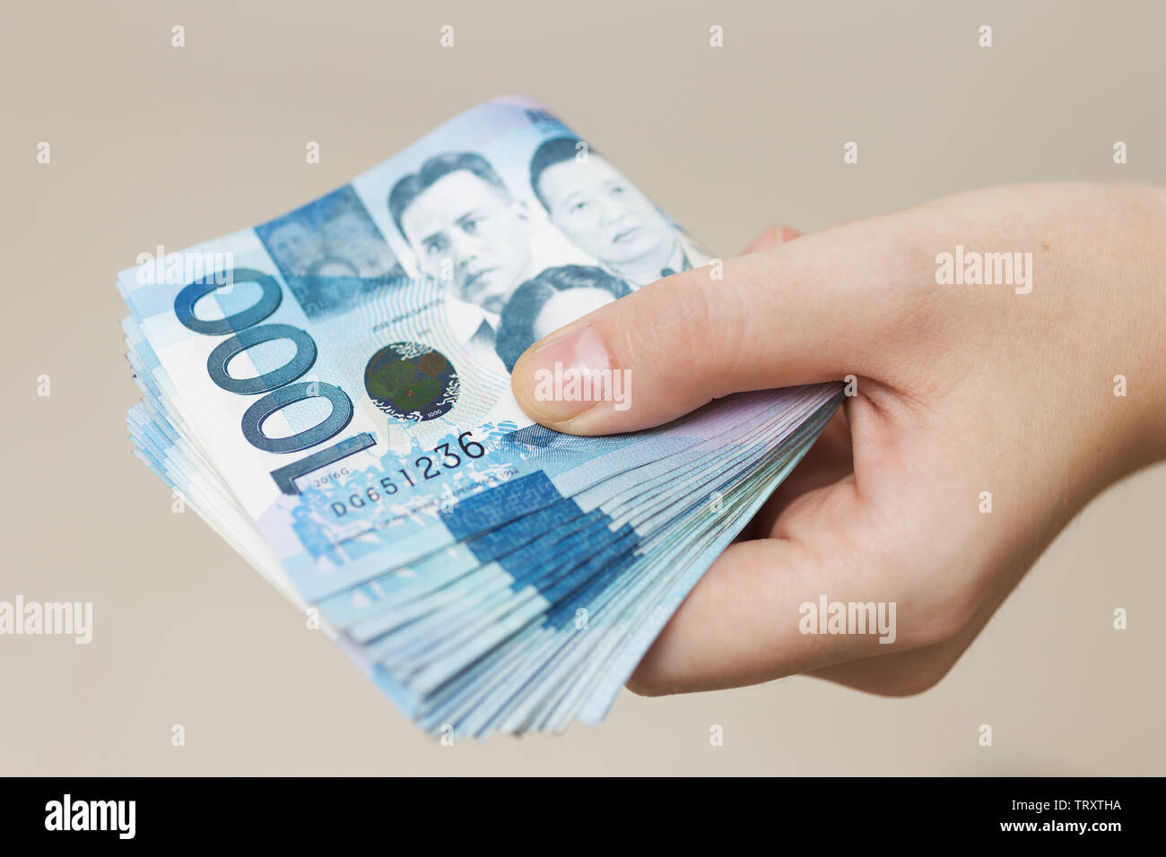 Mano che tiene ripiegato di blu denaro in contanti di mille Filippine pesos. Dando corrompere, pagare le bollette o ottenere lo stipendio. Pagamento il giorno! Foto Stock