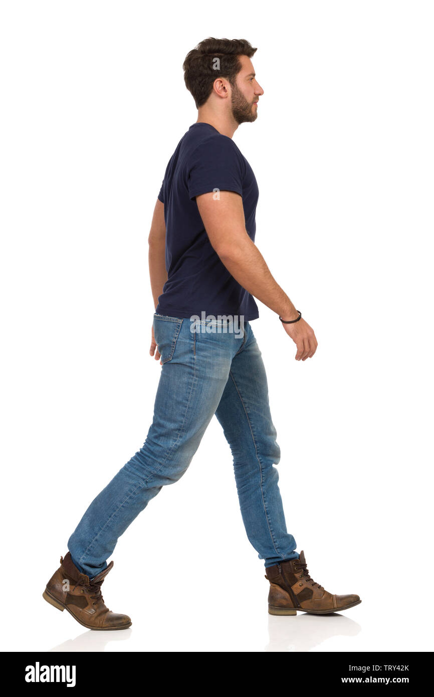 Uomo che cammina in jeans e maglietta blu e stivali è alla ricerca di  distanza. Vista laterale. Lunghezza completa studio shot isolato su bianco  Foto stock - Alamy