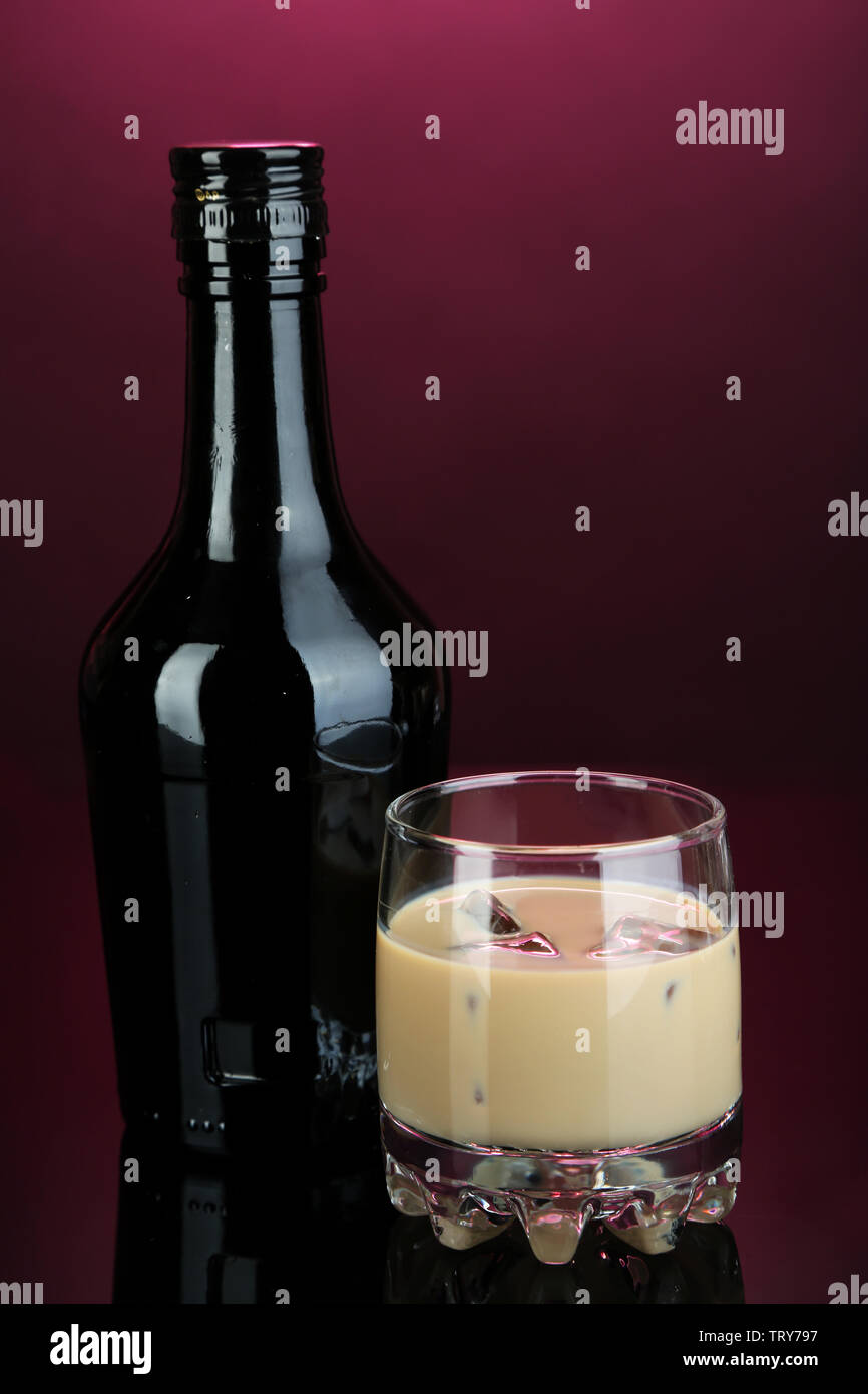 Il Baileys liquore in bottiglia e vetro su sfondo rosa Foto Stock