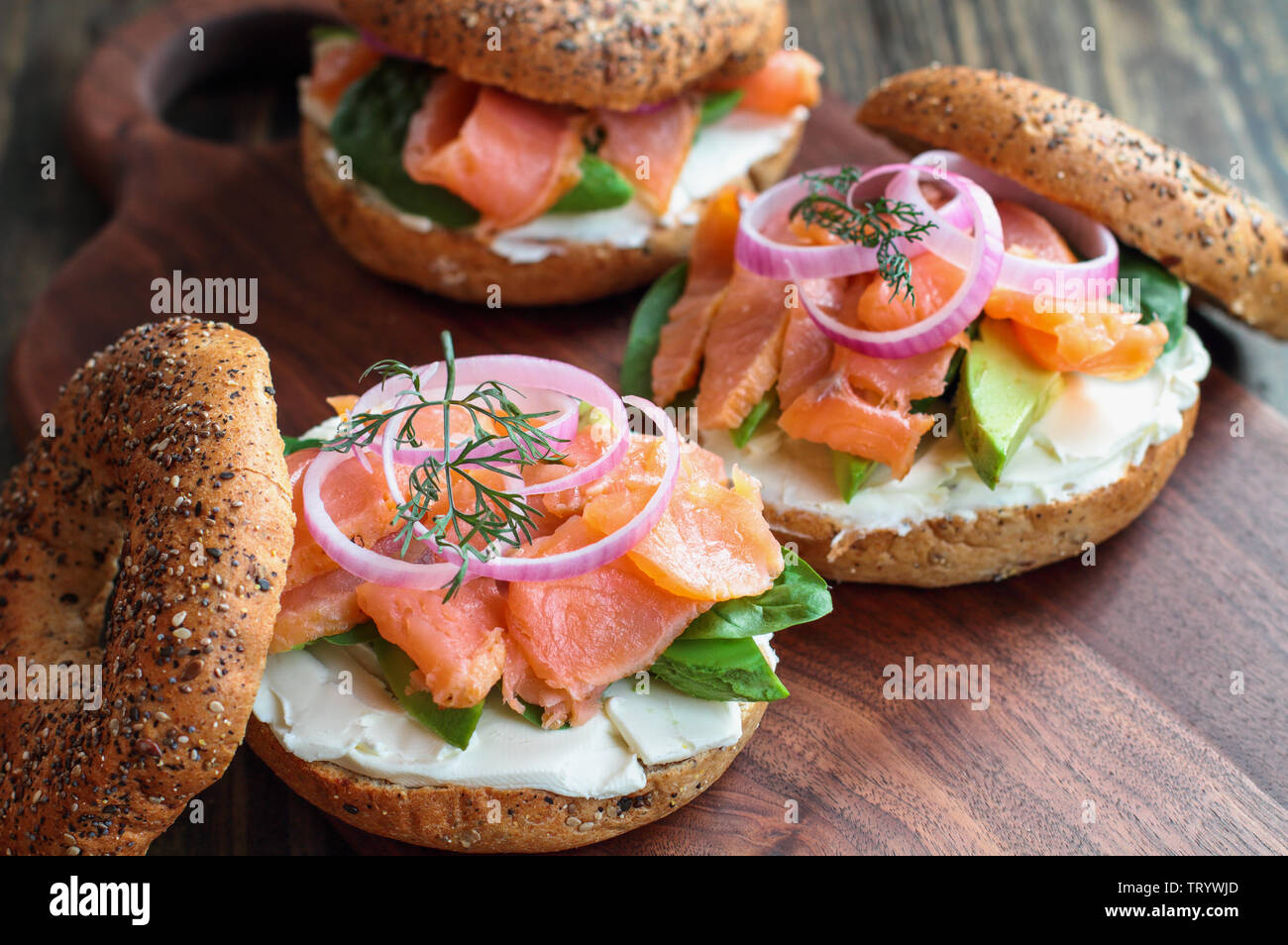 Lox - Tutto bagel con salmone affumicato, gli spinaci, le cipolle rosse, avocado e crema di formaggio su una tavola in legno rustico sfondo. Messa a fuoco selettiva. Foto Stock