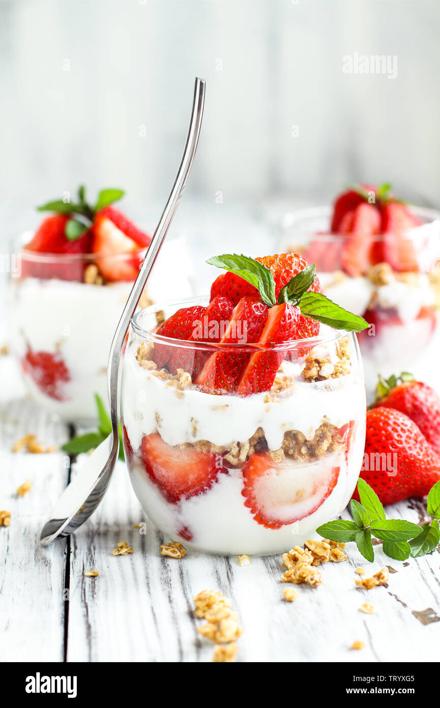 Sana colazione di fragola parfaits fatta con frutta fresca, yogurt e granola su un rustico tavolo bianco. Messa a fuoco selettiva. Foto Stock