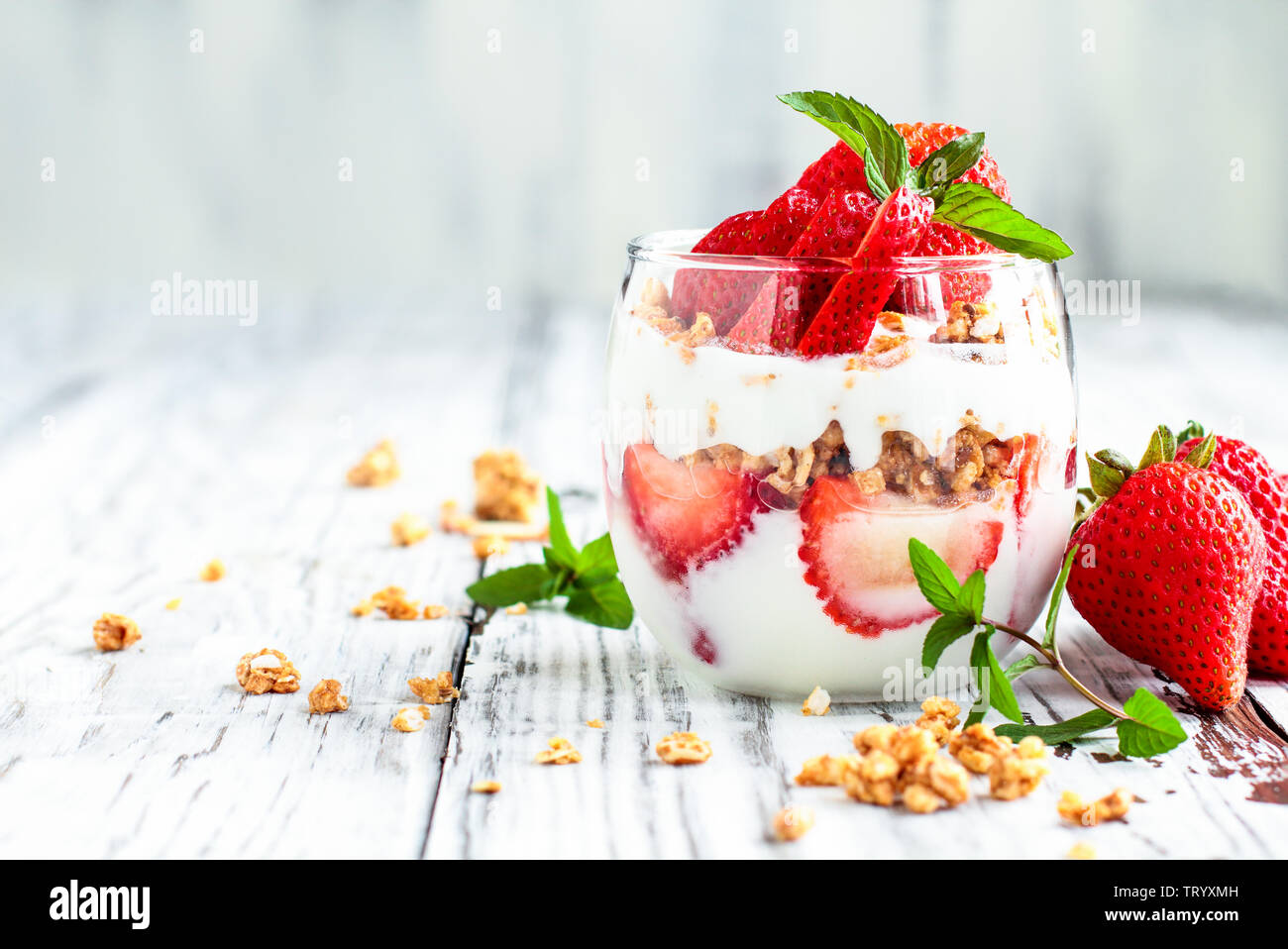 Sana colazione di fragola parfaits fatta con frutta fresca, yogurt e granola su un rustico tavolo bianco. Messa a fuoco selettiva. Foto Stock