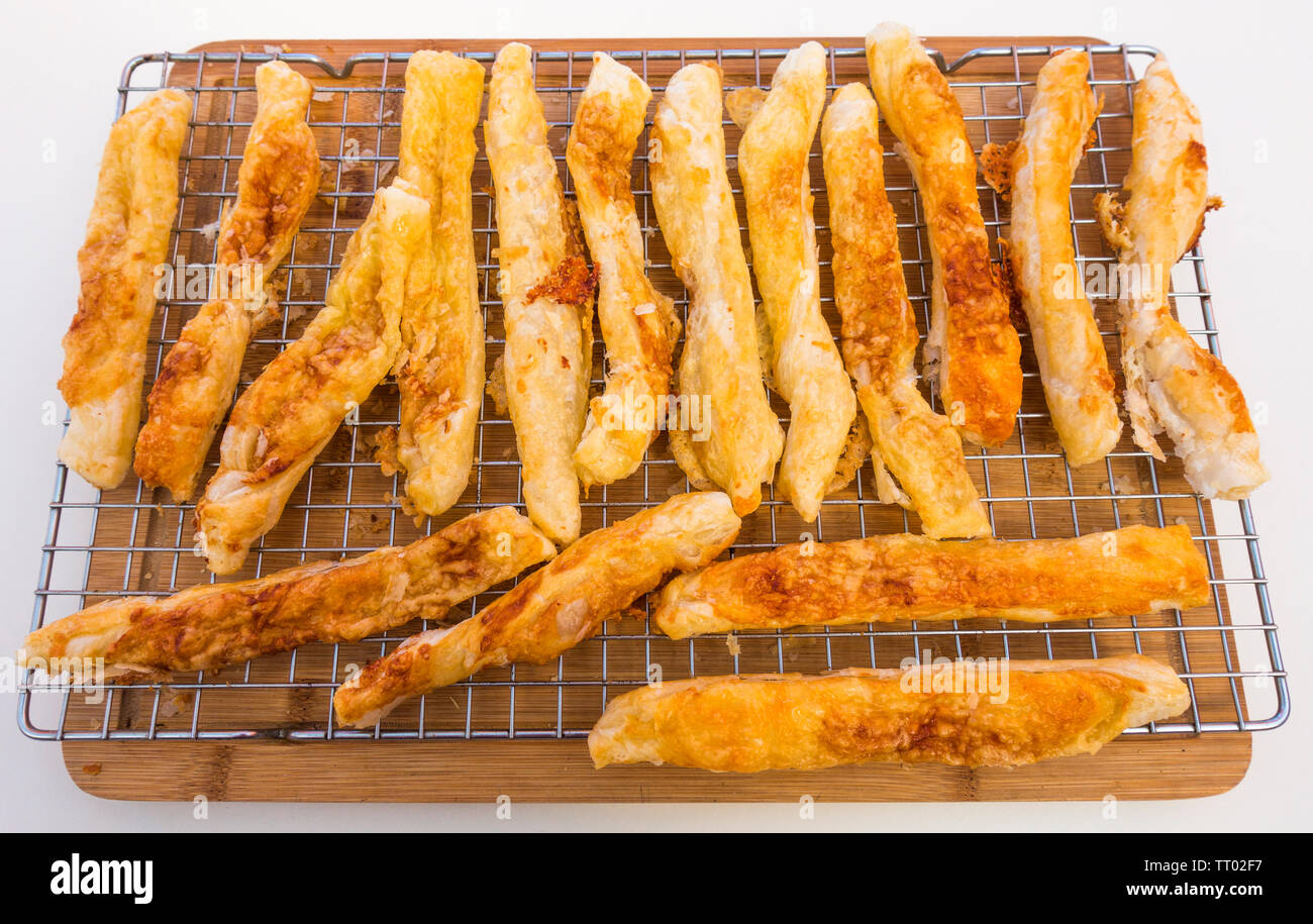 Un lotto di cotta al forno, fatti in casa, Golden, forma delle scaglie, formaggio bastoni in appoggio su una griglia di raffreddamento su un tagliere di legno. Foto Stock