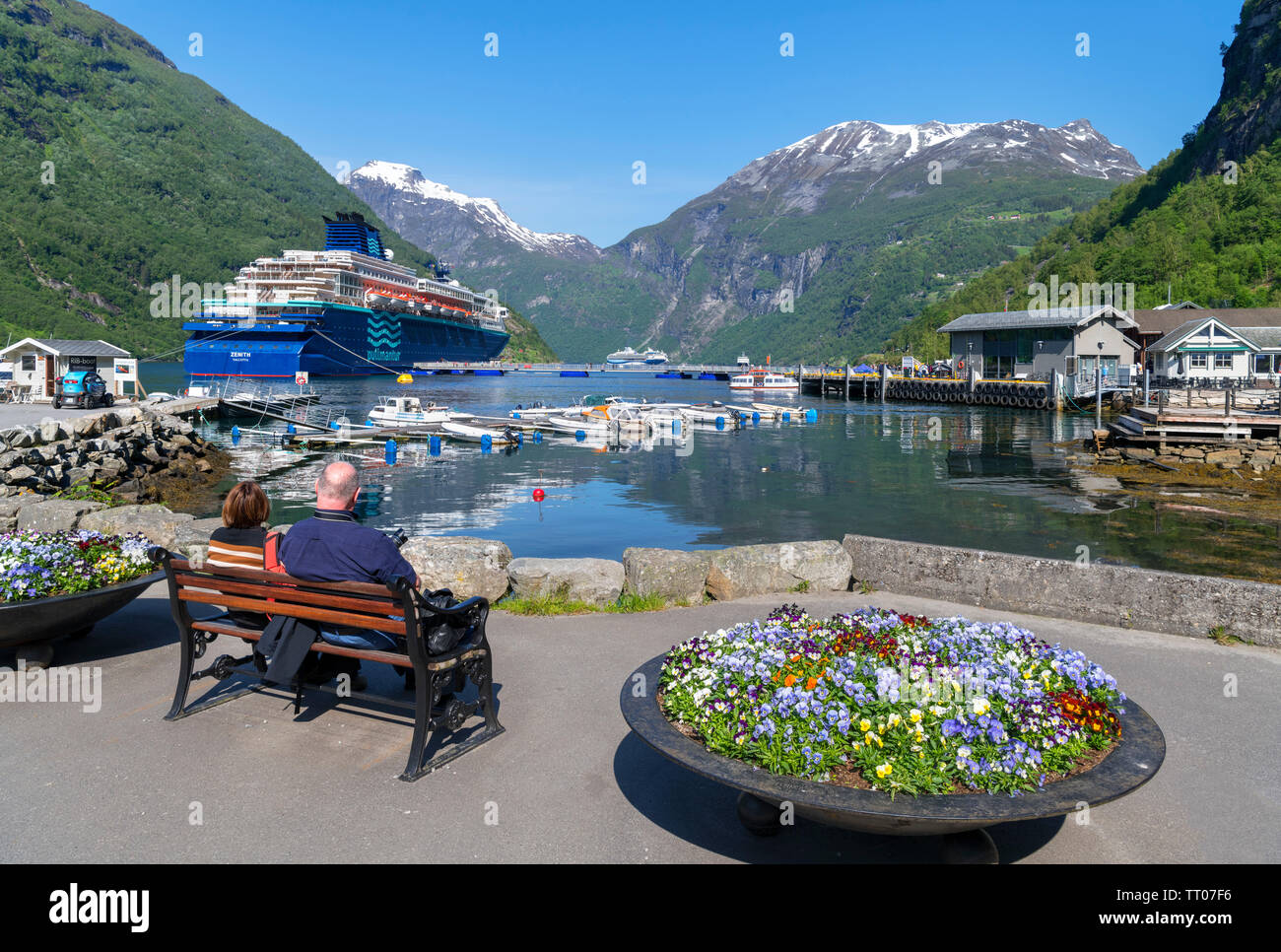 Coppia seduta su una panchina con la Pullmantur nave da crociera Zenith in porto dietro, Geiranger, Møre og Romsdal, Sunnmøre, Norvegia Foto Stock