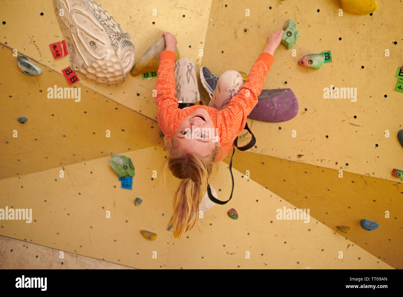 Ragazza giovane la scalata all'interno di una palestra di roccia sospesa a testa in giù e sorridenti mentre l apprendimento di nuove capacità Foto Stock