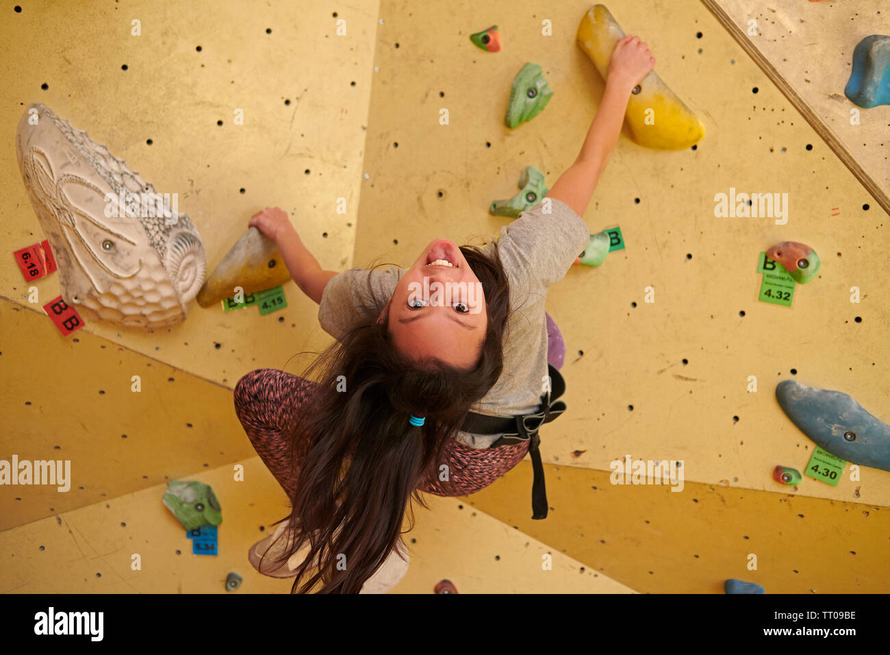 Ragazza giovane la scalata all'interno di una palestra di roccia sospesa a testa in giù e sorridenti mentre l apprendimento di nuove capacità Foto Stock