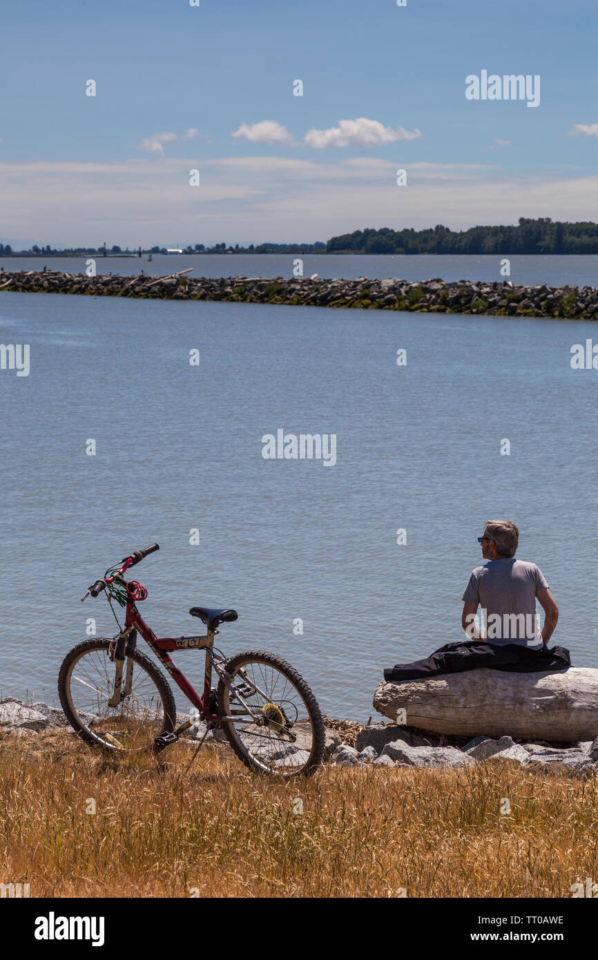 Ciclista in appoggio su un registro da oceano di Steveston British Columbia Foto Stock