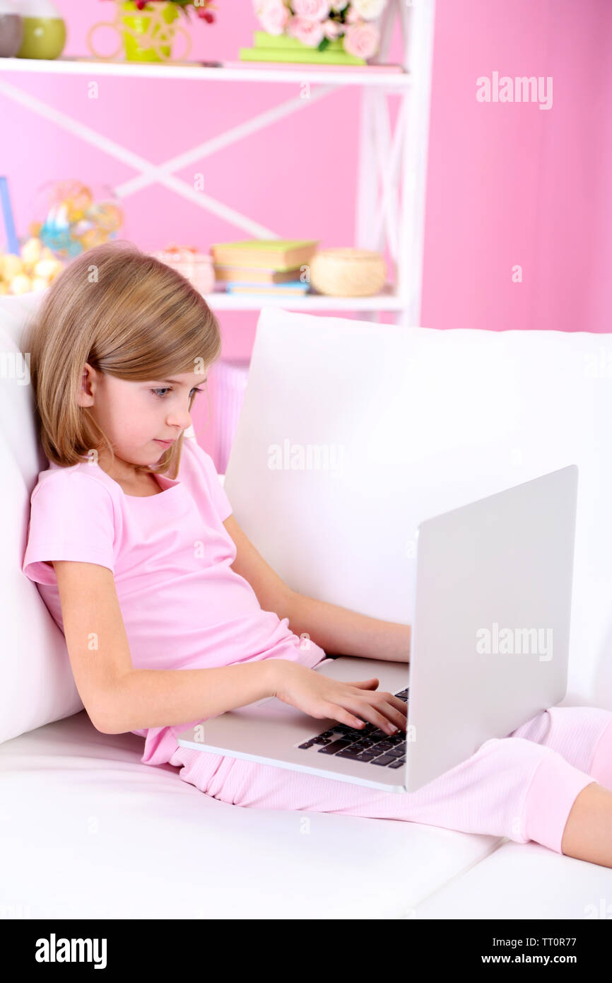 Poco ragazza seduta con il computer portatile sul divano in camera Foto Stock