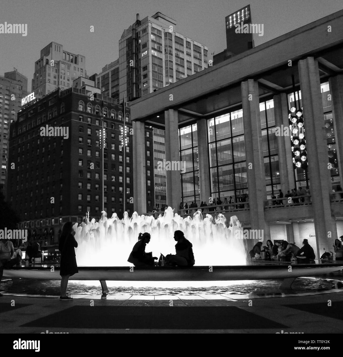 New York City - Giugno 10, 2016: due donne seduto di fronte alla fontana presso il Lincoln Center di notte con fontana illuminata creano il loro profilo. Als Foto Stock