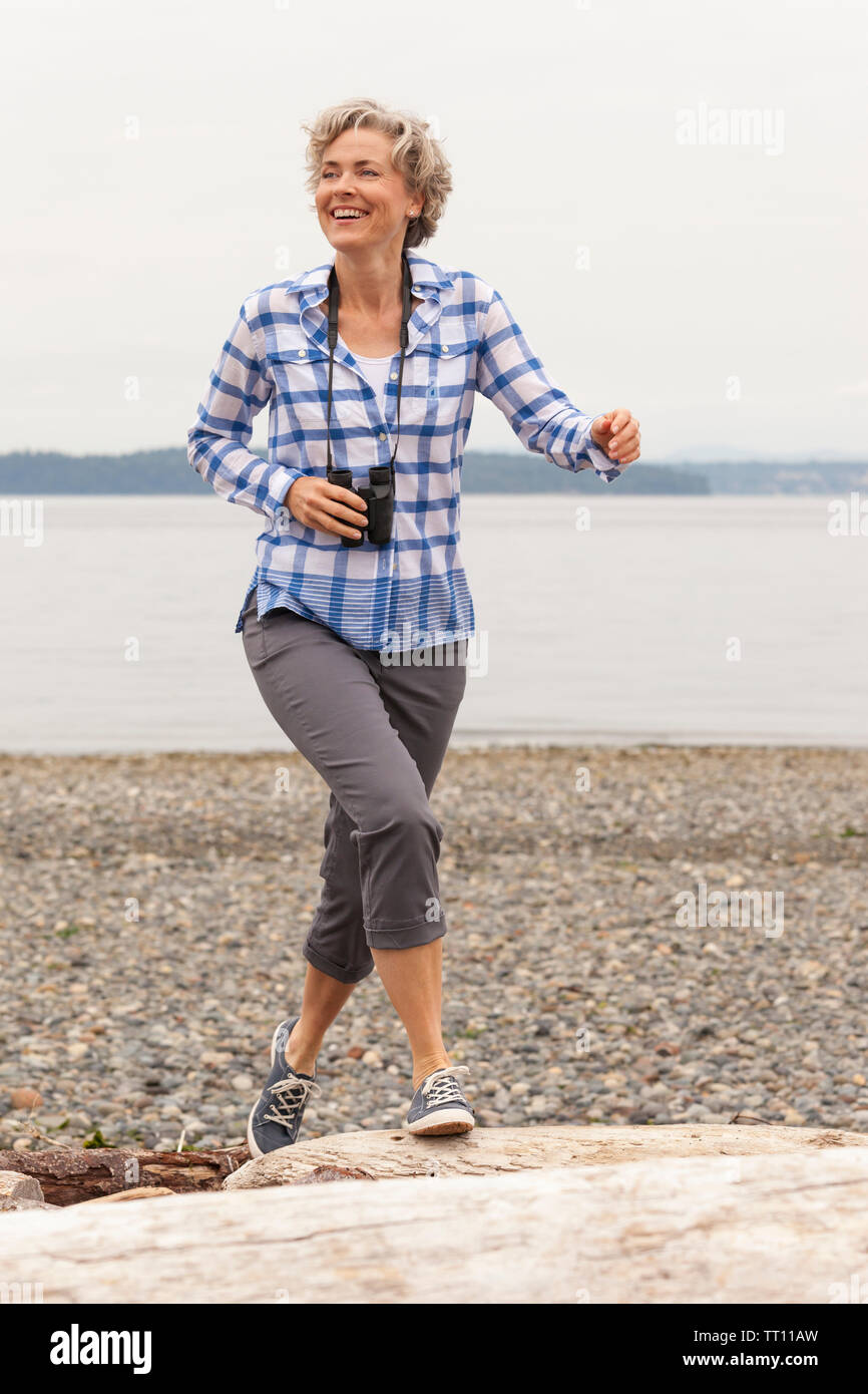 Bella, attivo, felice e sorridente donna di mezza età con un binocolo per godersi la natura all'aperto sulla spiaggia Foto Stock