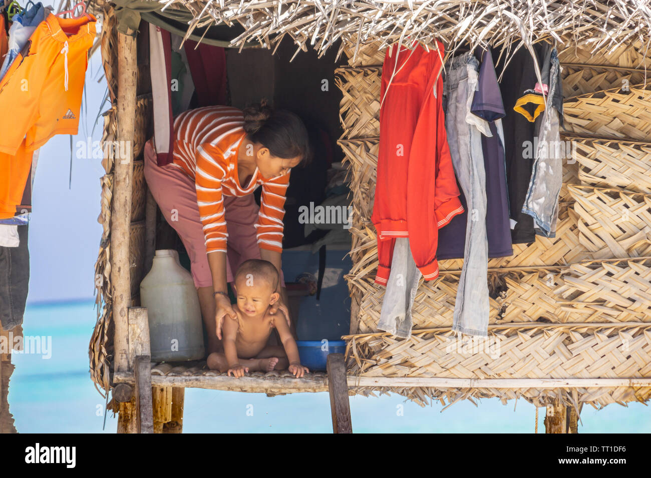 SEMPRONA BORNEO - Maggio11 2019; donna e madre di Bajau Laut tribale gruppo etnico con un bambino piccolo in modo porta di palm thatch home su palafitte sulla piccola tr Foto Stock