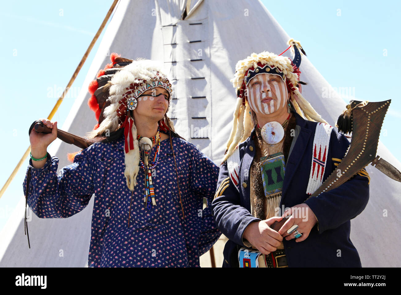 Indiani del Nord America stand con arma vicino a wigwam contro il cielo blu. La ricostruzione di native american life su Mosca festival storici Foto Stock