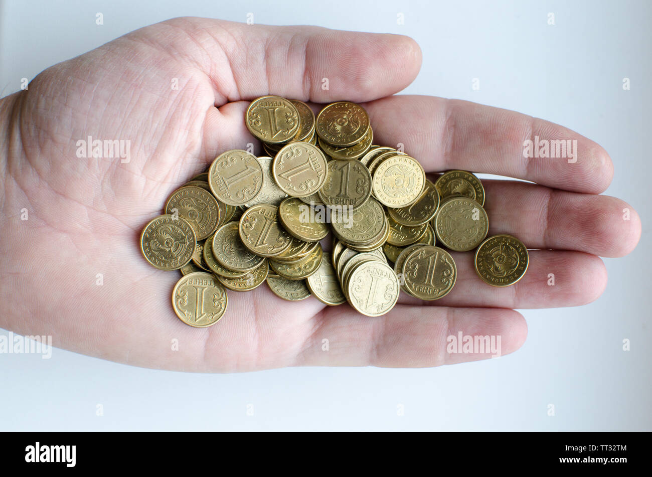 Man mano tenendo un sacco di monete con un valore nominale di uno tenge su uno sfondo luminoso Foto Stock