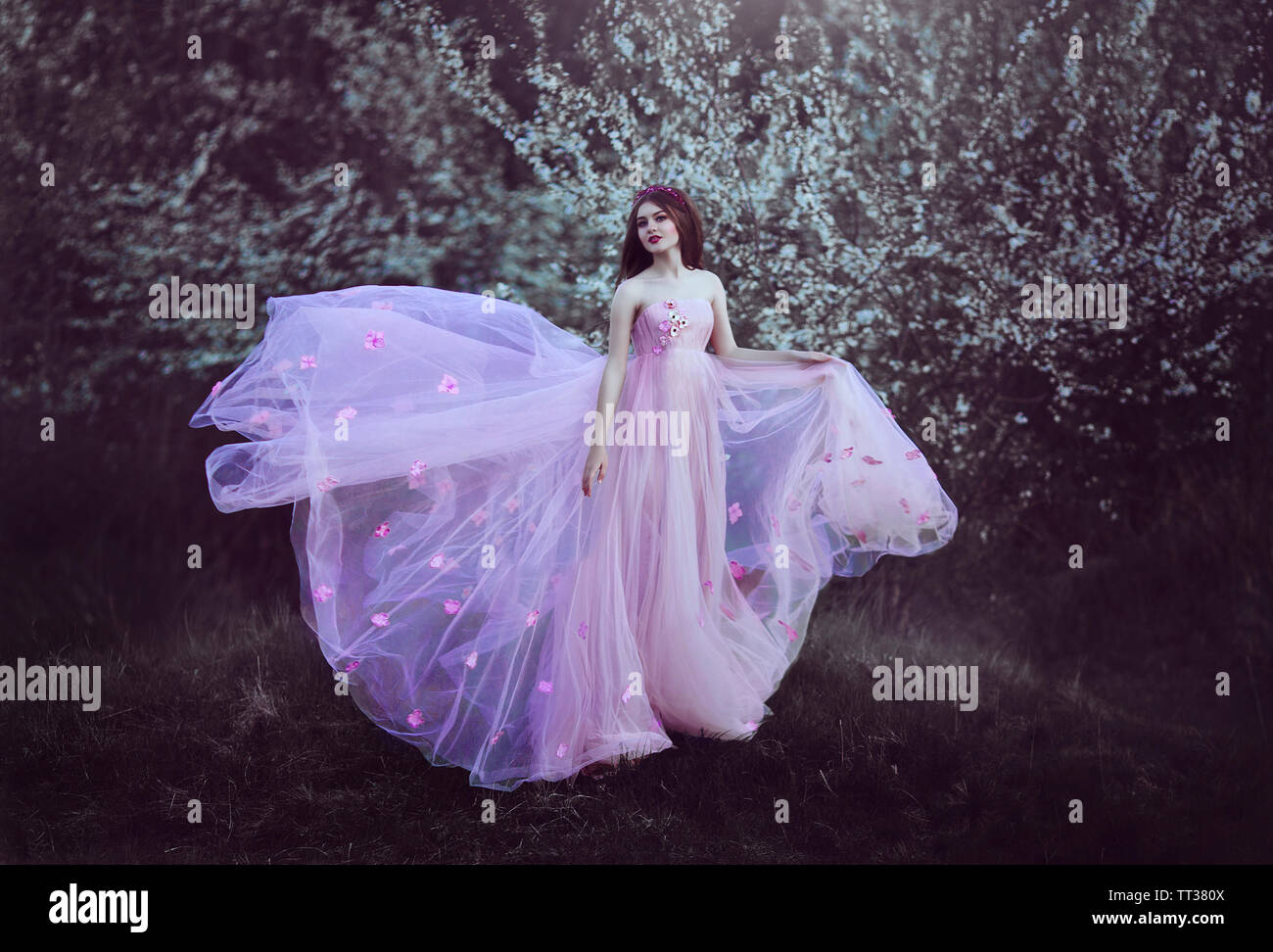 Bella ragazza romantica con capelli lunghi in fairy lungo abito rosa in piedi vicino a fioritura tree.Fantasia arte. Colori creativi e lavorazione artistica. Foto Stock