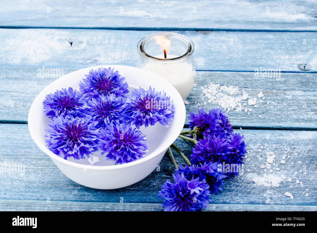 Blue cornflowers giacciono in acqua in una vaschetta bianca in prossimità di una candela che brucia contro lo sfondo di colore blu vecchie schede madri. close-up Foto Stock