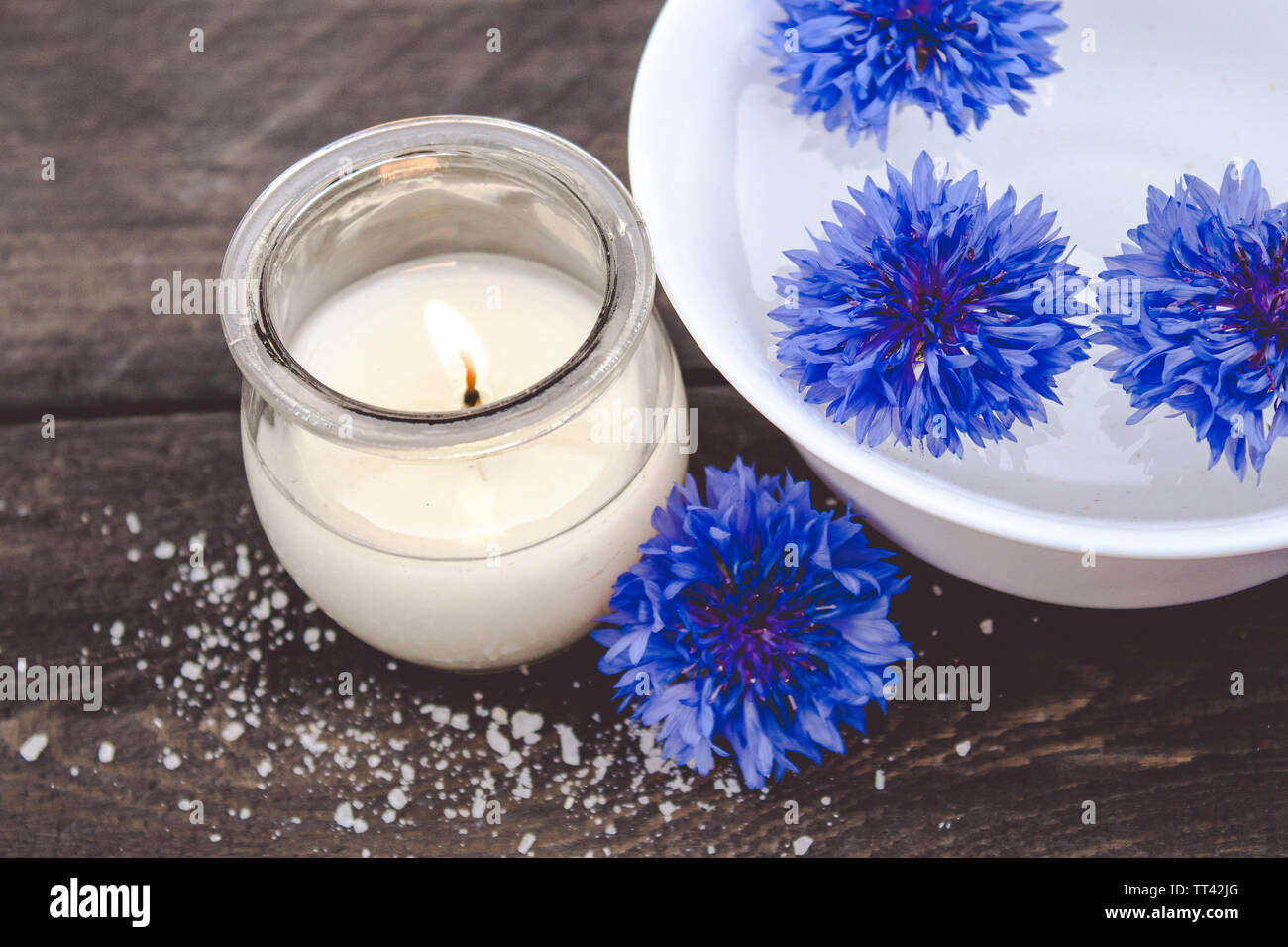 Blue cornflowers giacciono in acqua in una vaschetta bianca in prossimità di una candela che brucia sullo sfondo di vecchie schede madri. close-up Foto Stock