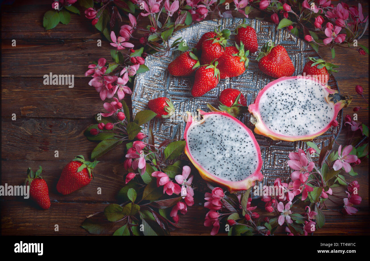 Cibo flatlay background - vuoto in legno scuro con scheda dragon frutta, fragole e fiori di colore rosa, copia spazio per il testo Foto Stock