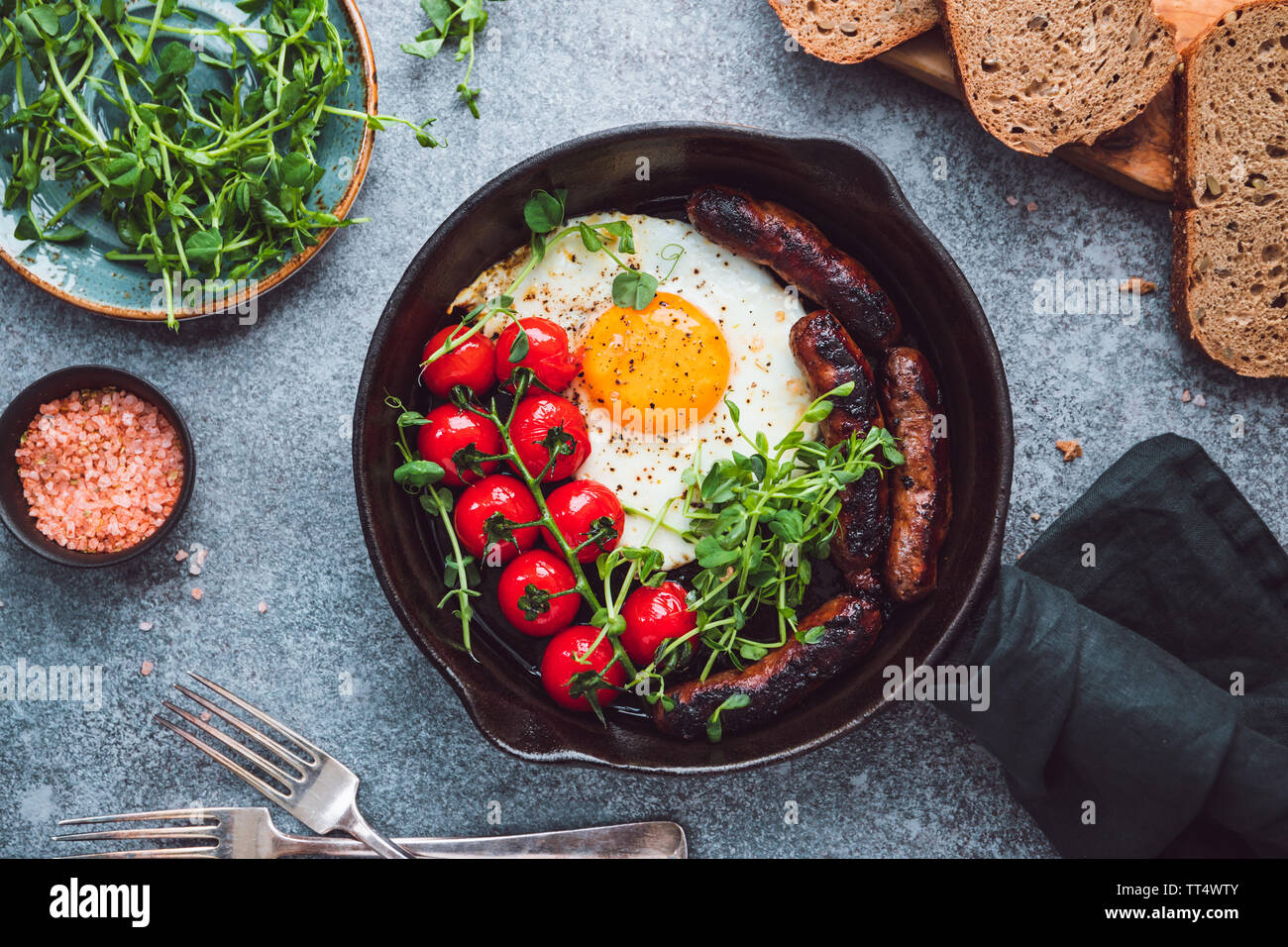 Il momento della colazione, uovo fritto con salsicce e pomodori ciliegia in un nero padella di ferro, servita microgreens. Foto Stock