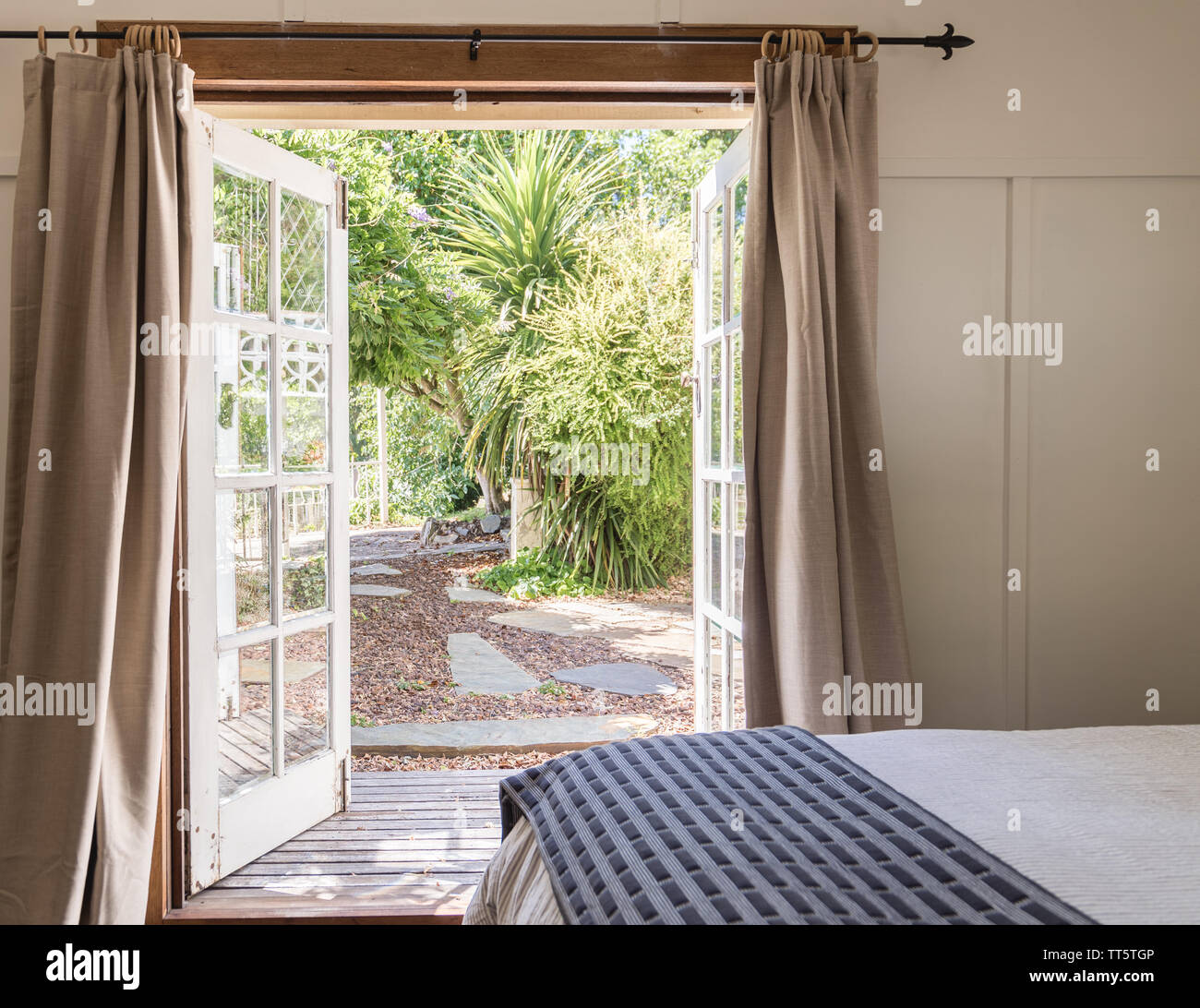 Letto in una camera da letto con aprire porte francesi con tende su un cortile e un lussureggiante giardino verde Foto Stock