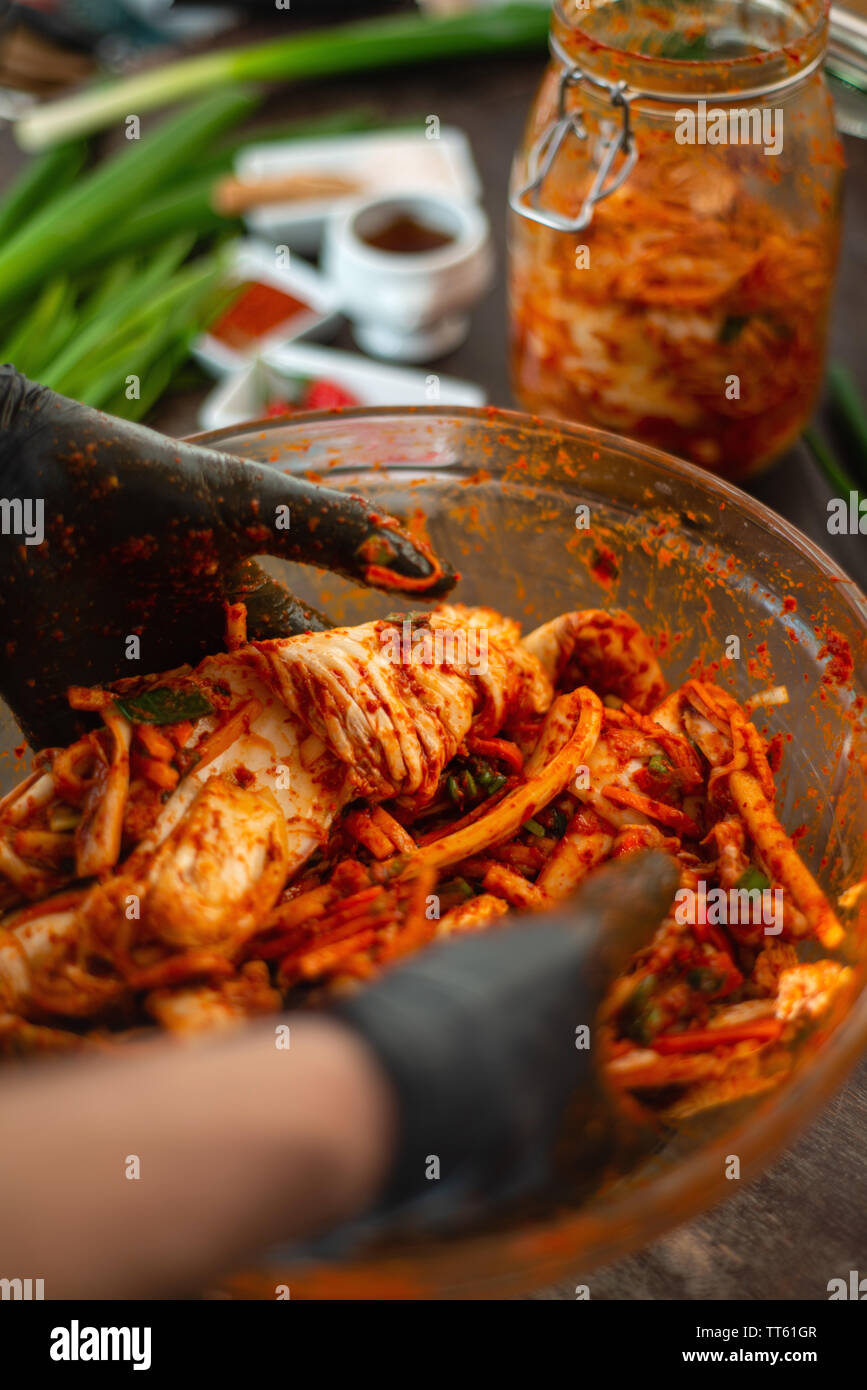 Mani guanti in preparazione kimchee piccante un sano preferito coreano fermentato condimento. Colorato e delizioso. Foto Stock