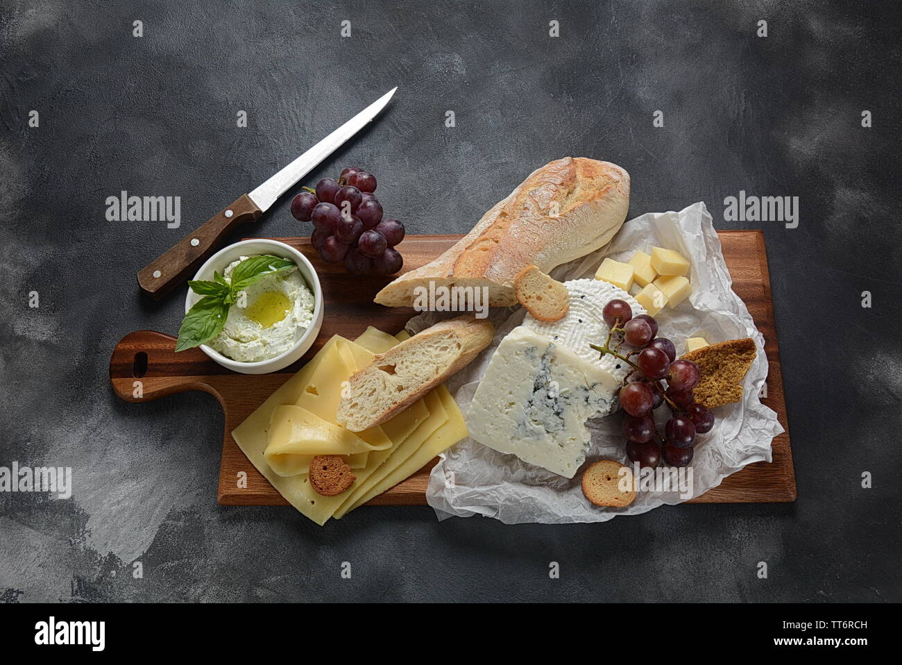 Un vassoio di formaggi con formaggi assortiti, uva, spuntini su sfondo scuro. Italiano, formaggio francese motorino di avviamento Foto Stock