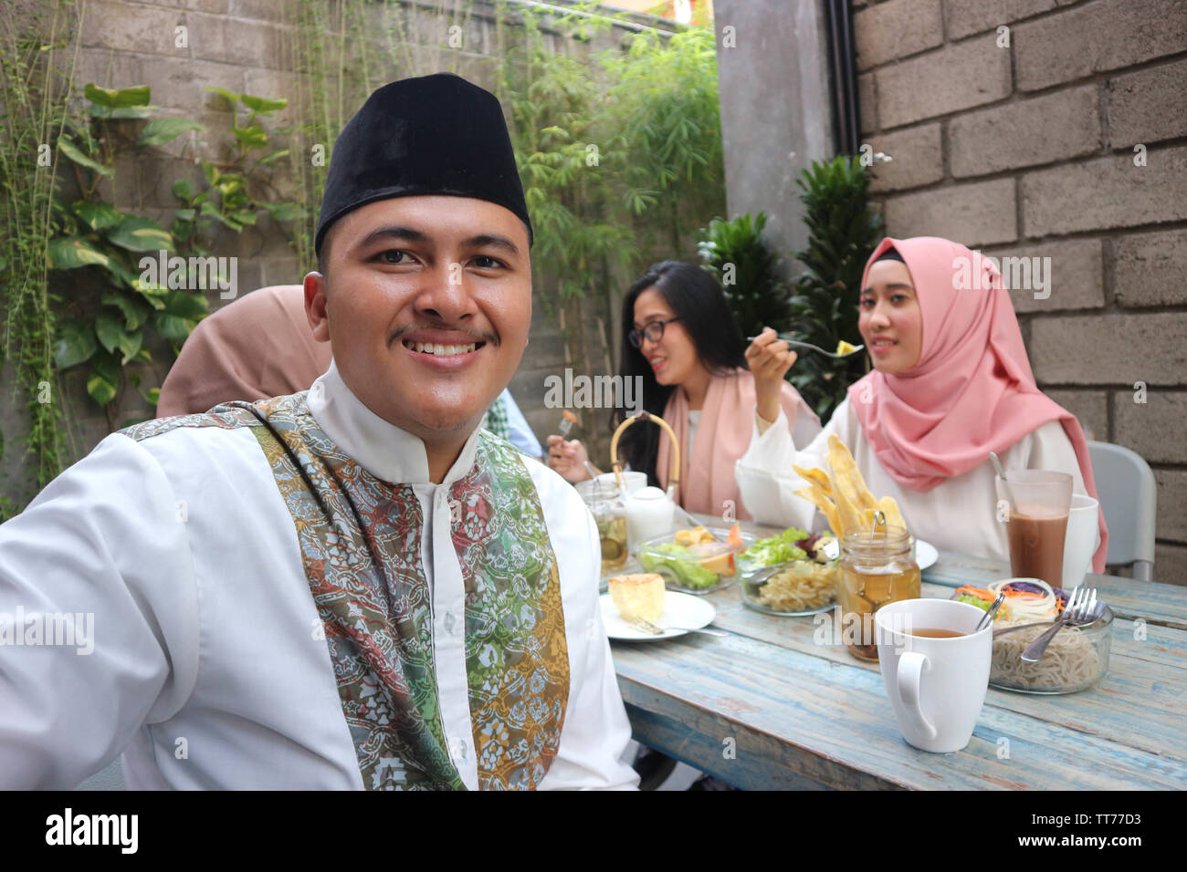 Il Portrait di uomo musulmano guardando la fotocamera mentre altri pople mangiare durante il ramadan celebrazione, rompere il digiuno Foto Stock