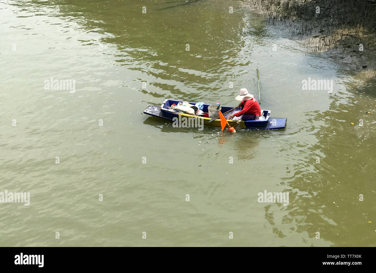Vecchia donna con paddle su una barca mentre si verifica la rete nel fiume, Thailandia. Foto Stock