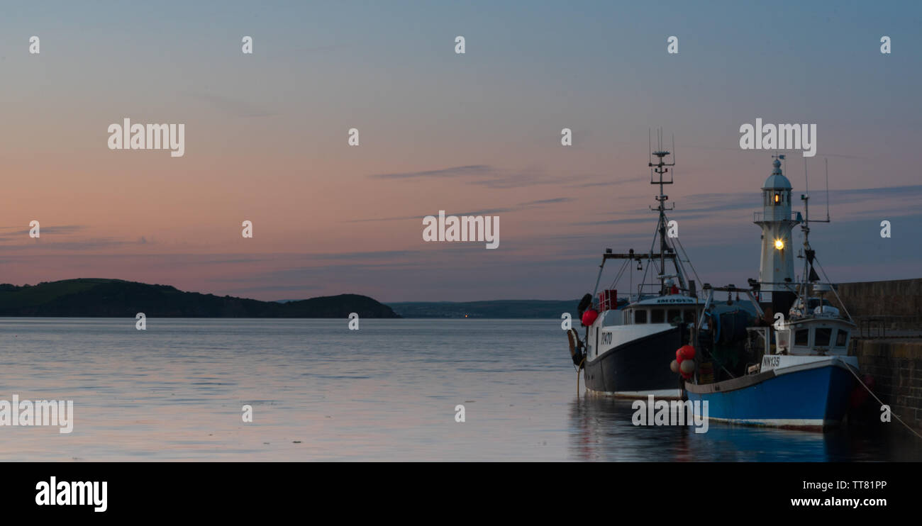 Night Shot di due barche da pesca ormeggiate nel porto di Mevagissey, Cornwall, Regno Unito con il porto di scintillanti luce in background. Foto Stock