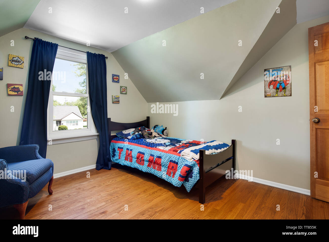 Un giovane ragazzo in camera con Thomas il treno set letto, una sedia blu nell'angolo e alcune immagini di supereroi sulla parete. Foto Stock