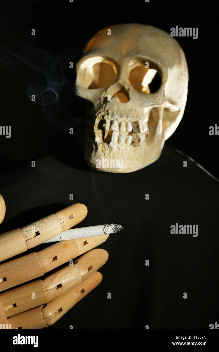 Scull umano e a mano in legno con la sigaretta su sfondo scuro Foto Stock