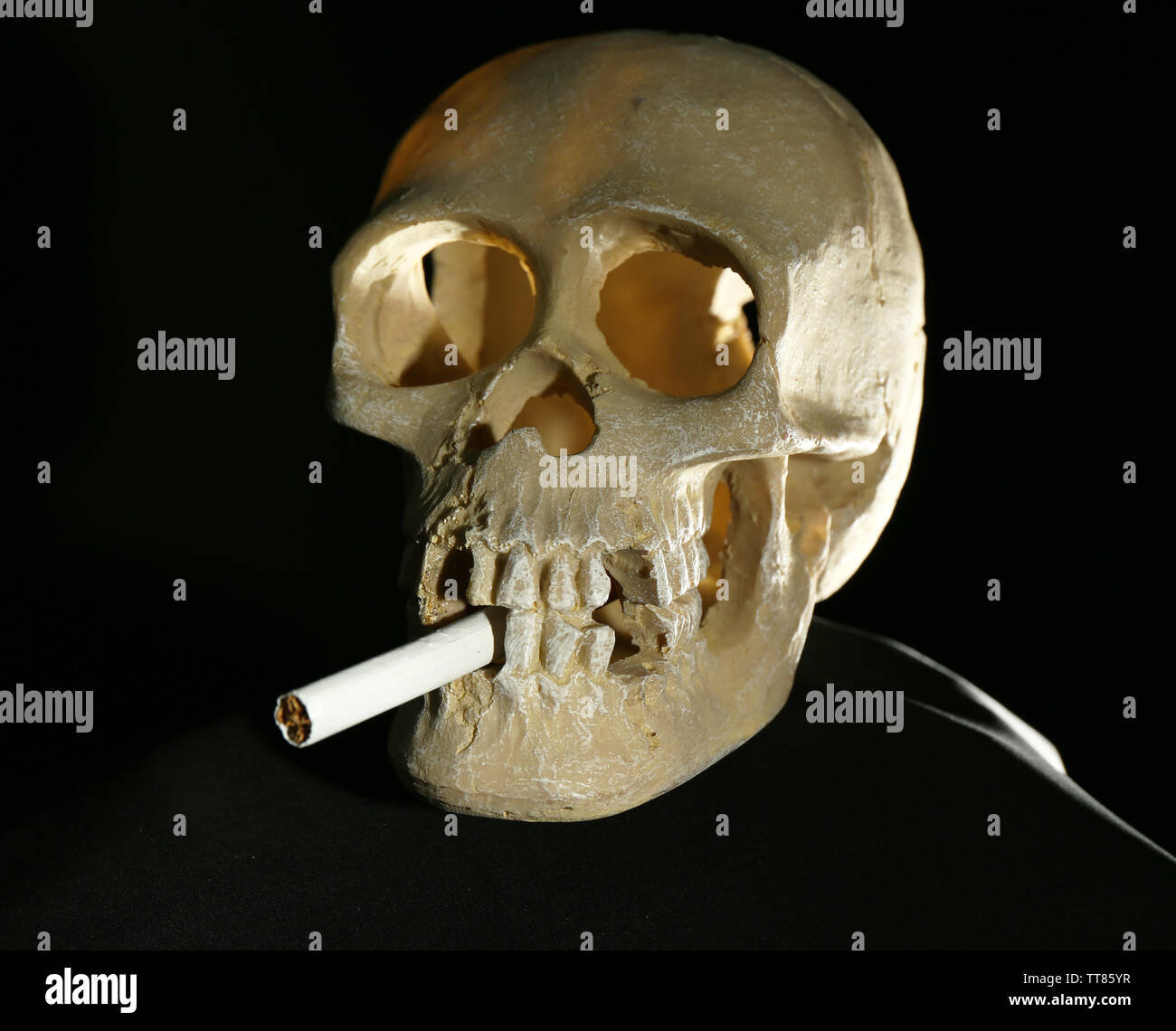 Scull umano e a mano in legno con la sigaretta su sfondo scuro Foto Stock